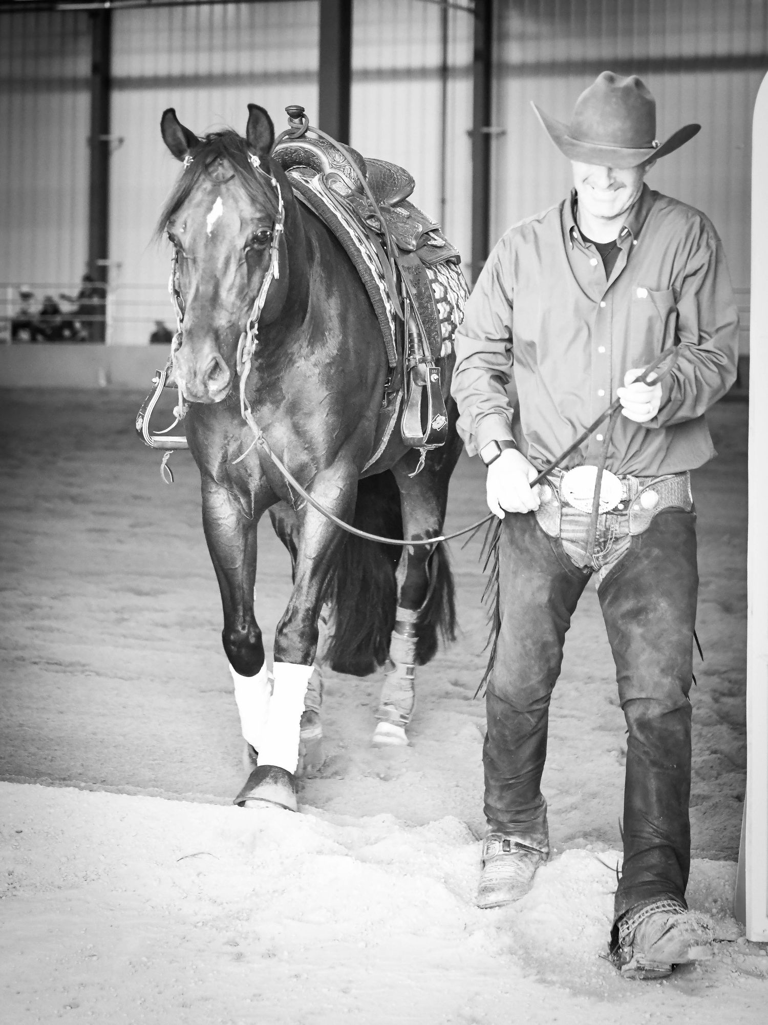 Black and white photo of saddled horse with rancher in barn.