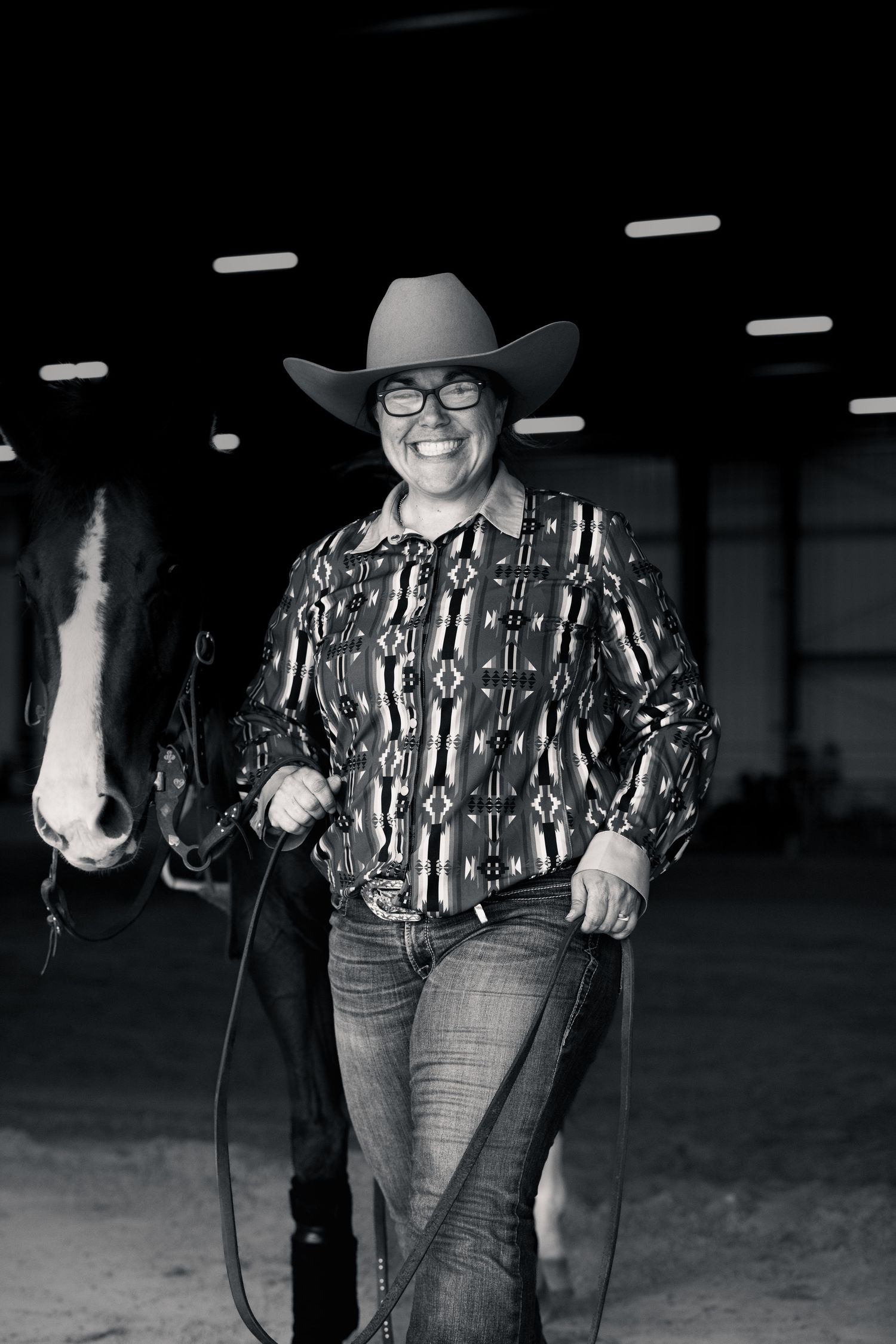 Western-style portrait of a person in cowboy attire and hat in dark indoor setting.