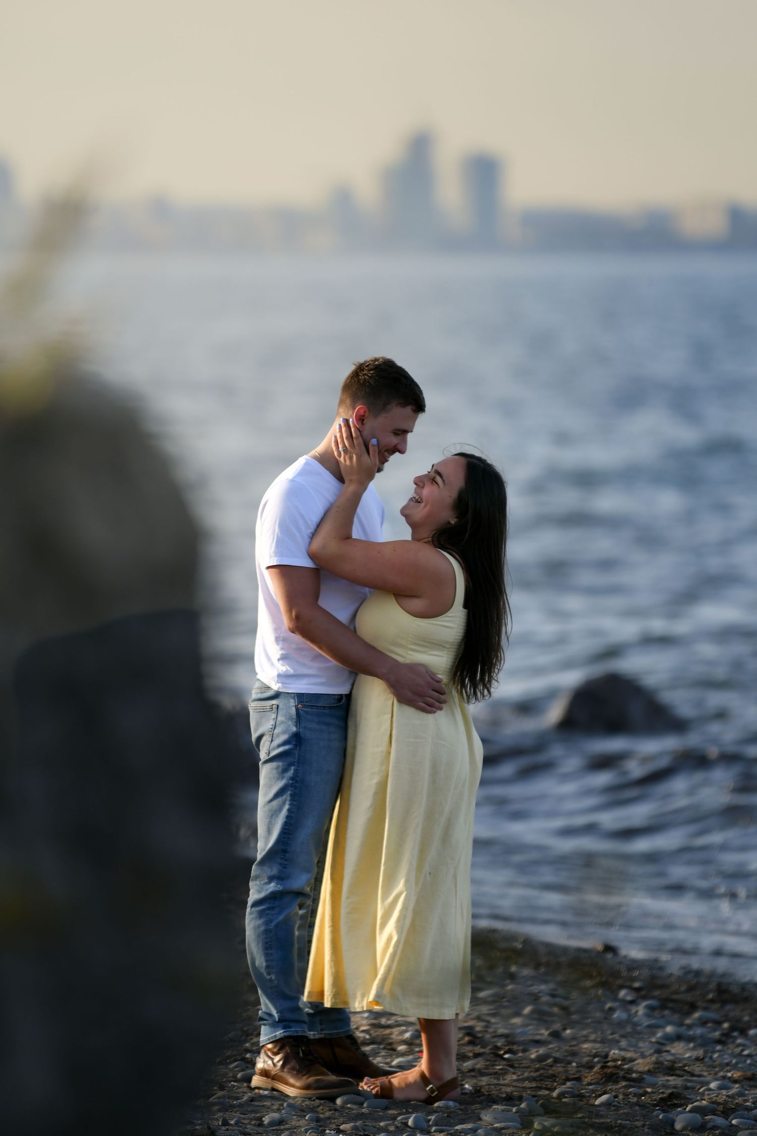 A couple shares an intimate moment on a rocky shoreline during sunset.