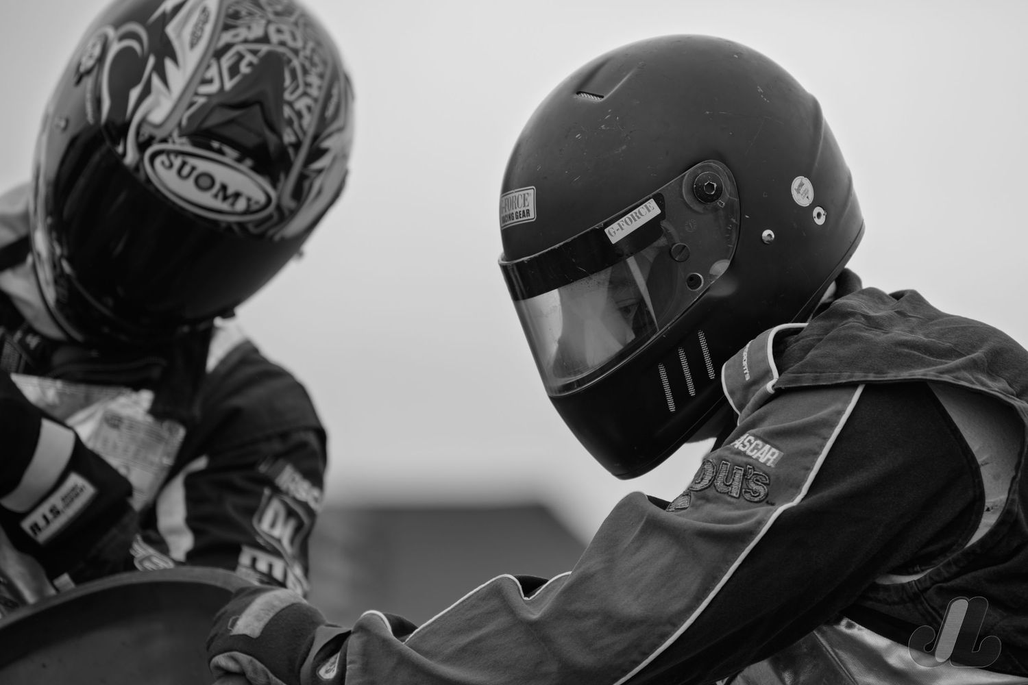 View of two individuals in flame retardant safety equipment and helmets, pouring race gasoline.