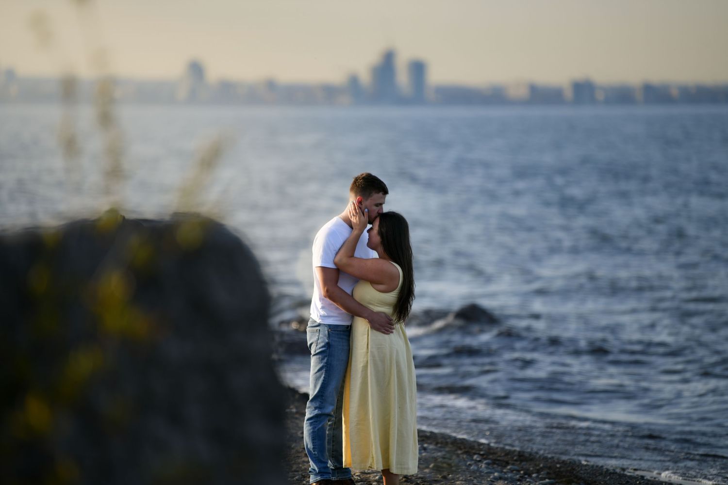 A romantic waterfront scene at sunset with a city skyline visible in the distance.