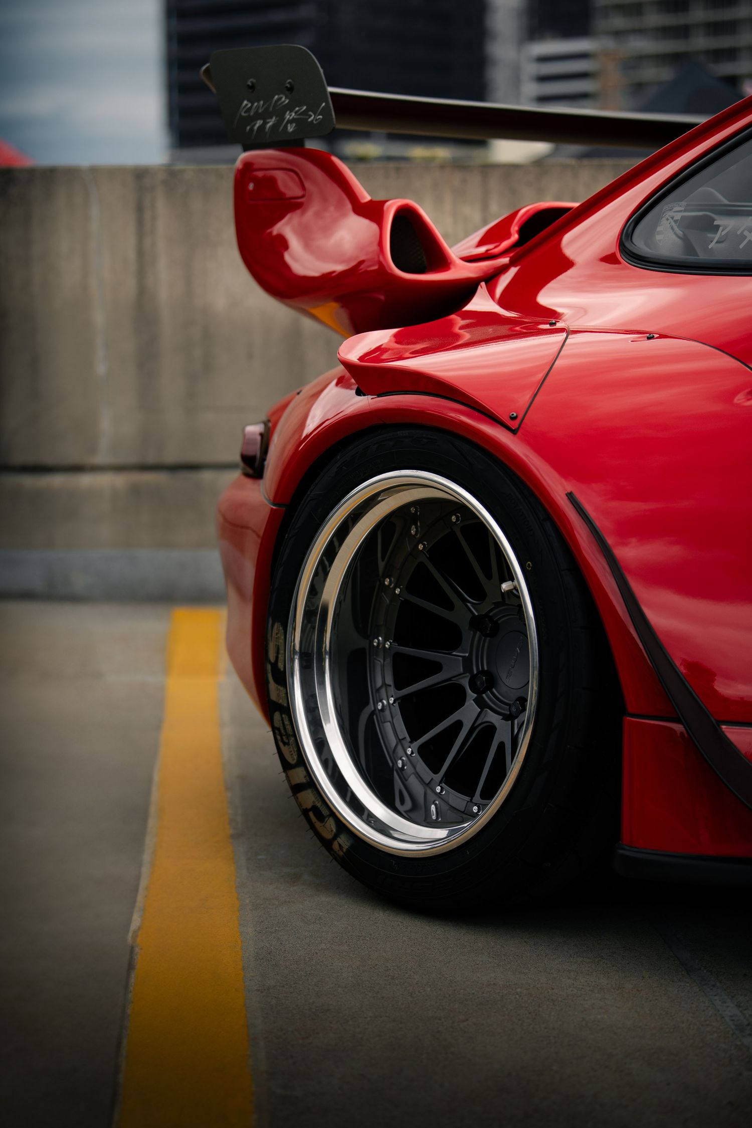 Close-up detail shots of a red RWB custom wide-body wheel setup and suspension in a parking garage.