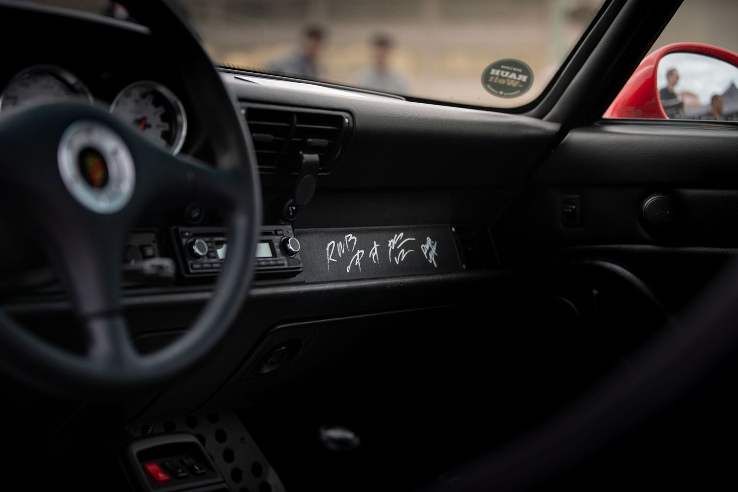 Dark interior view of a porsche dashboard and steering wheel with ambient lighting, signed by Akira Nakai from RWB.