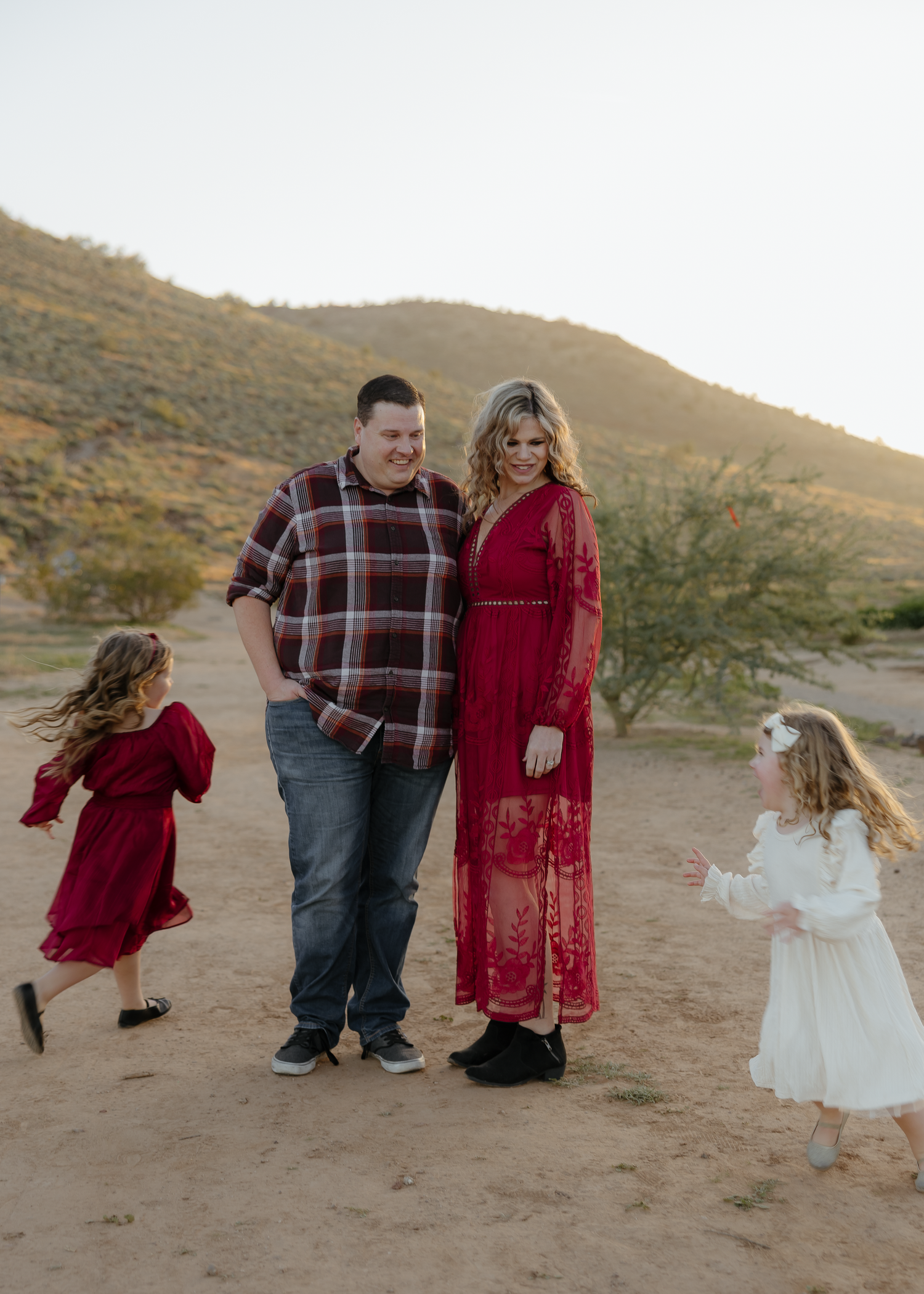 A couple and two young girls enjoy a sunny desert landscape during a family photo session.