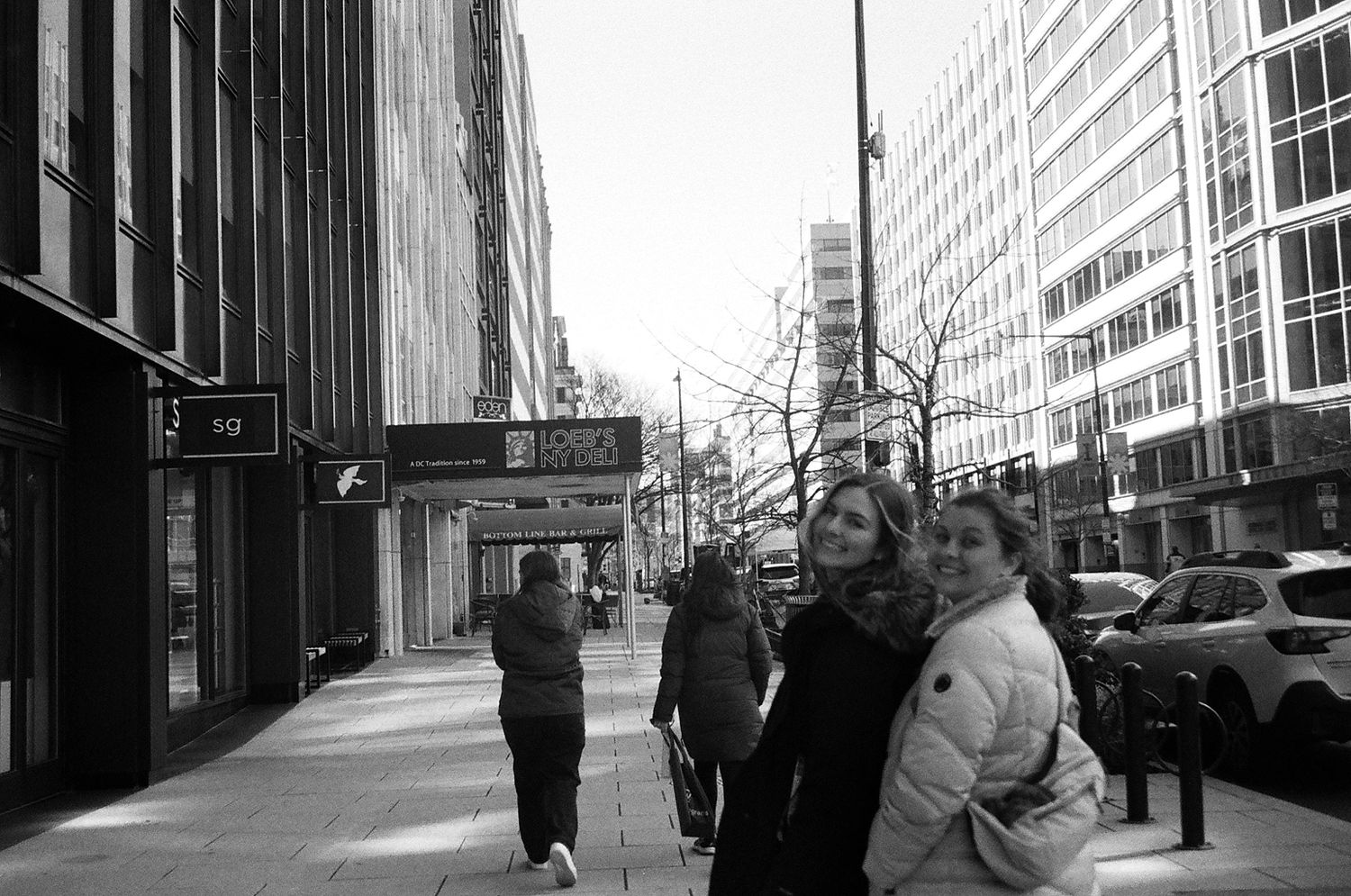 Black and white street photography of people walking on urban sidewalk with tall buildings.