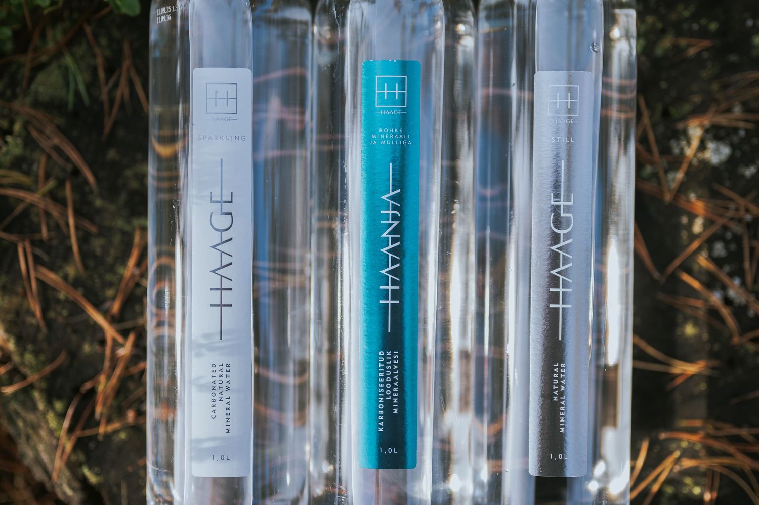 Five HAANJA water bottles with vertical labels displayed side by side outdoors.