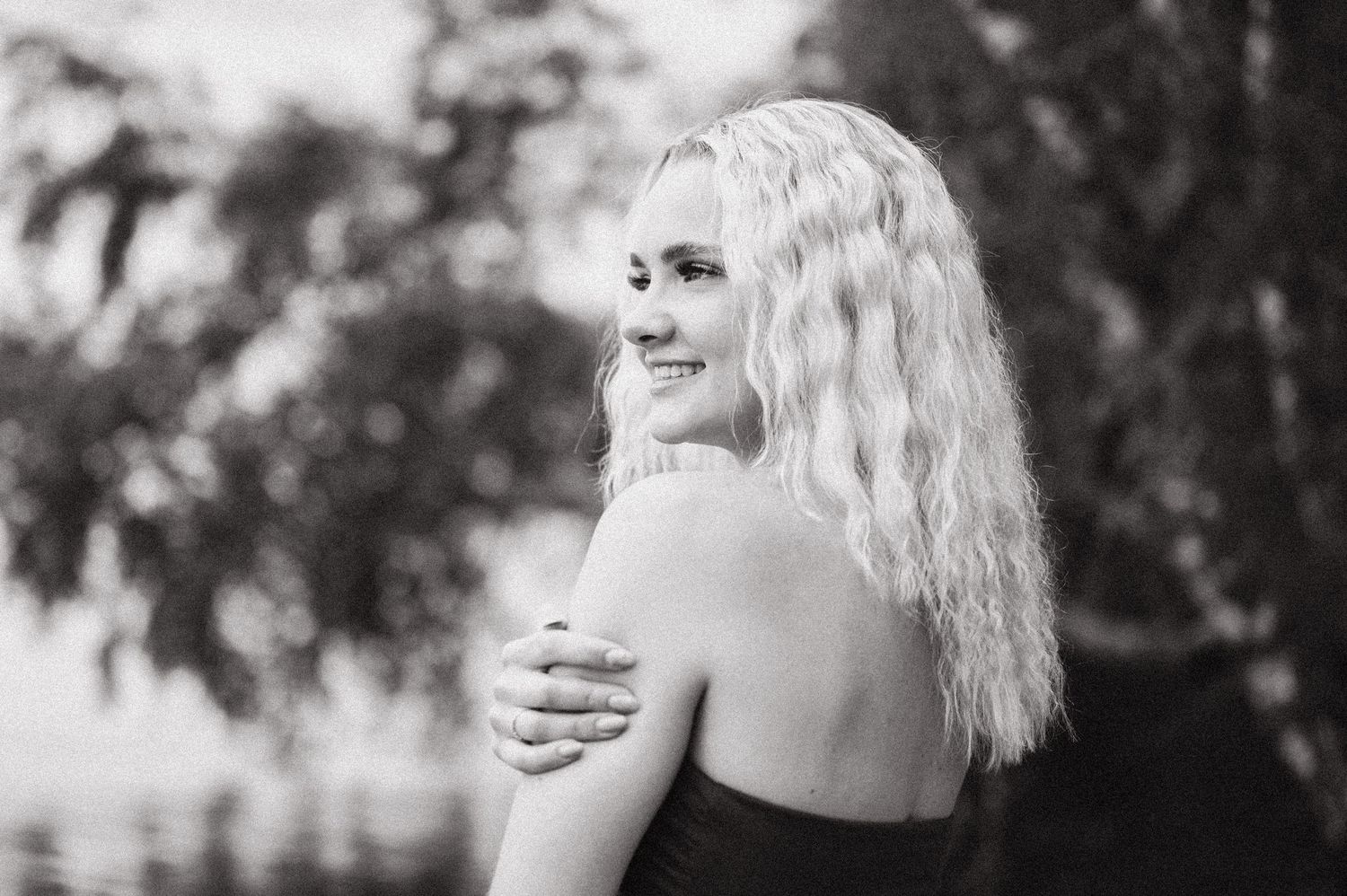 Black and white portrait of a smiling blonde woman looking over her shoulder outdoors.