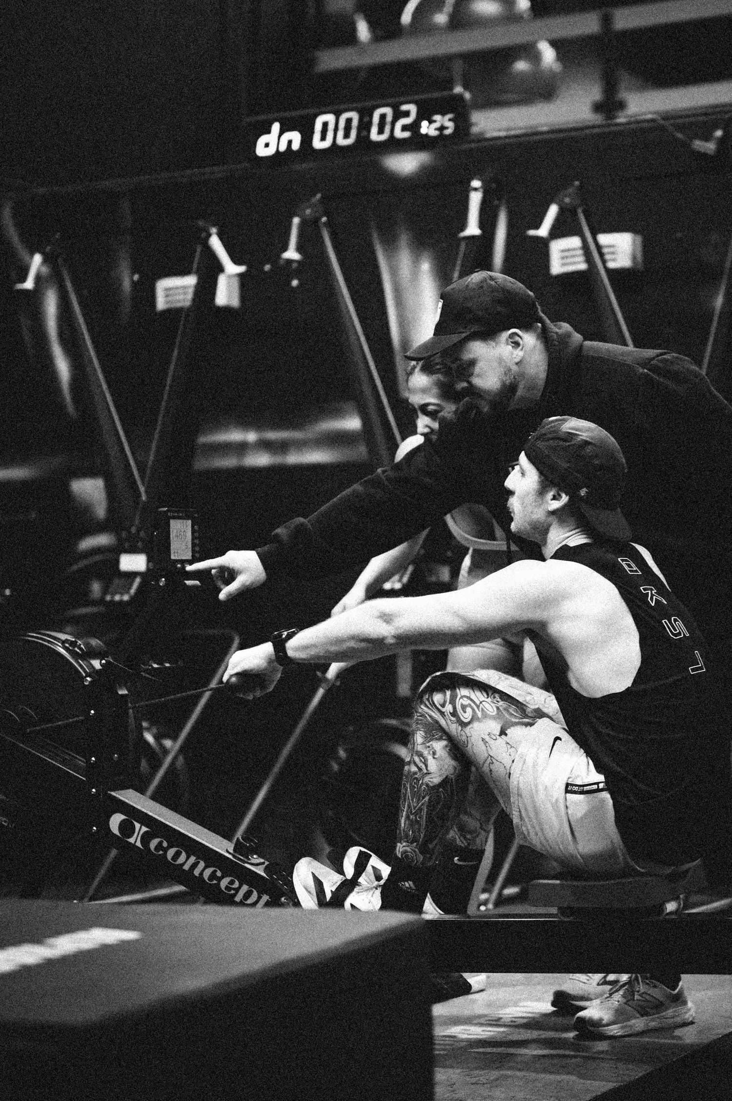 Coach guiding athlete on proper rowing machine technique in a black and white gym photo.