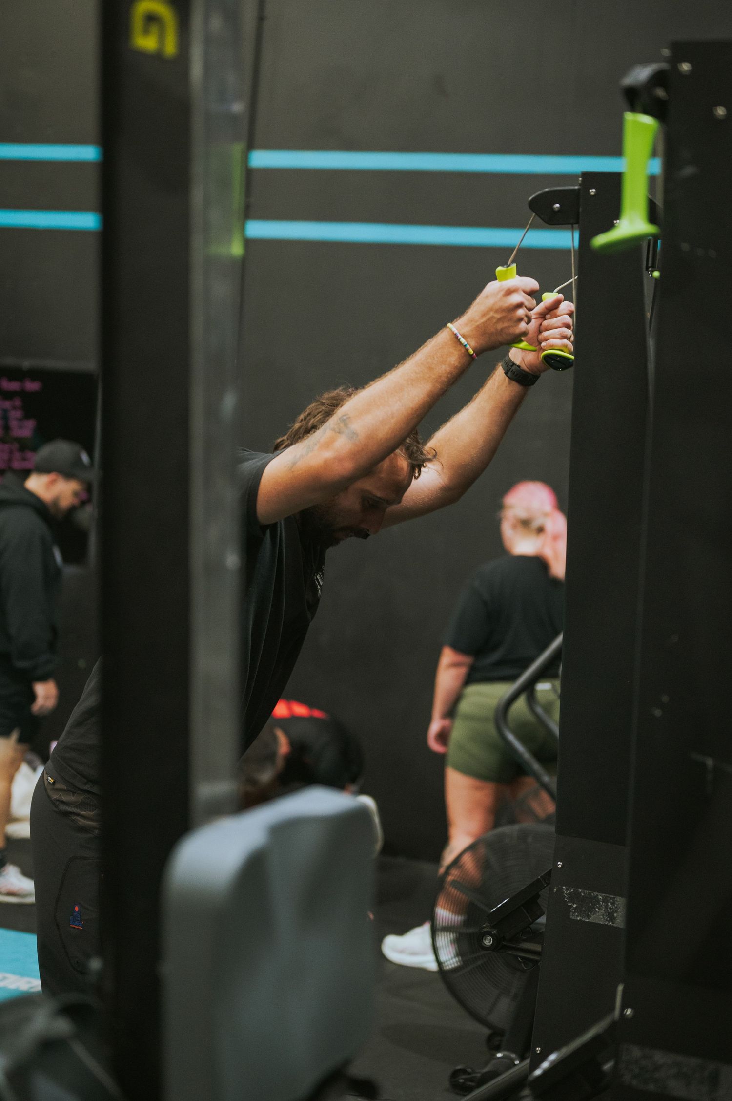 Male athlete using cable machine for lat pulldown exercise in a dark modern gym.