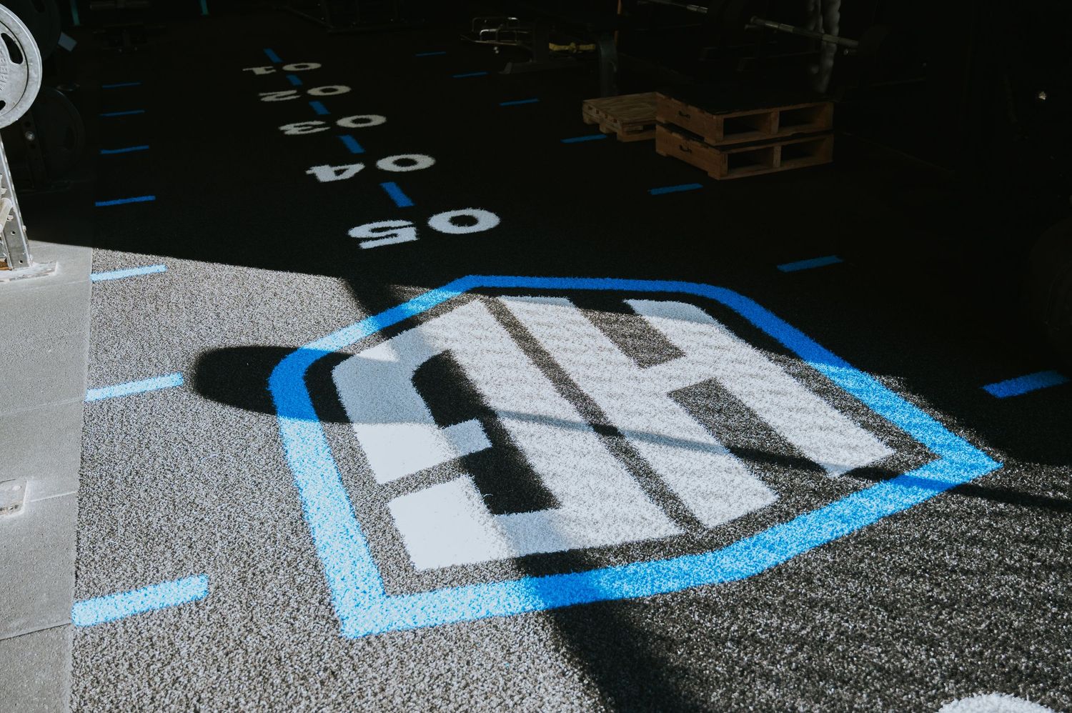 Blue and gray gym floor logo painted on dark rubber flooring with distance markers.