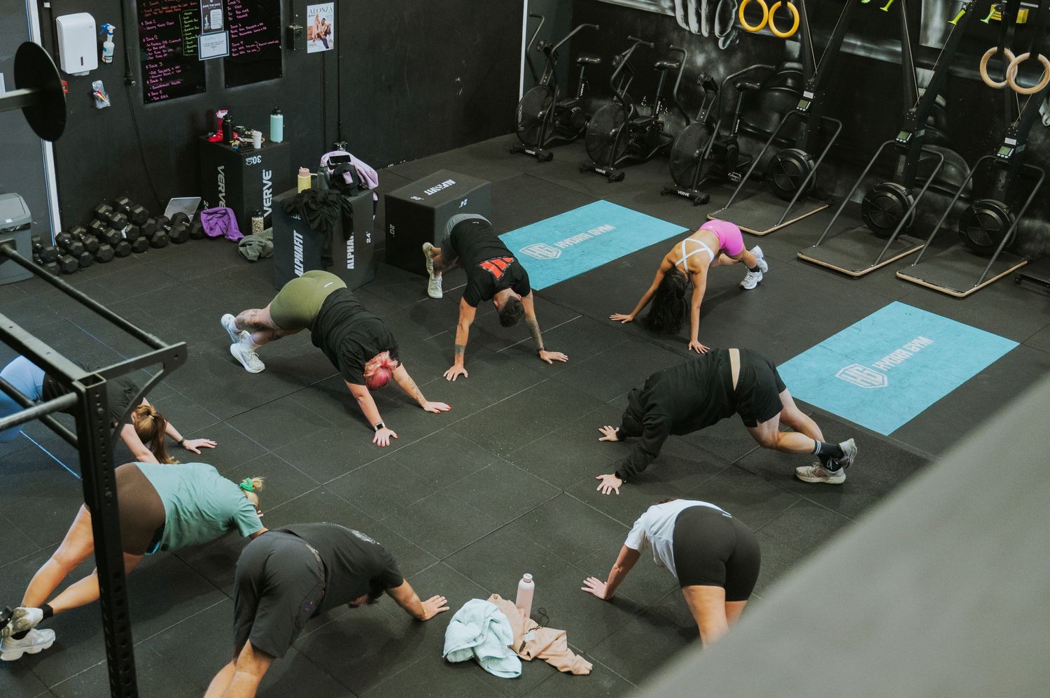 Group fitness class performing bear crawl exercises on blue mats in a dark gym.