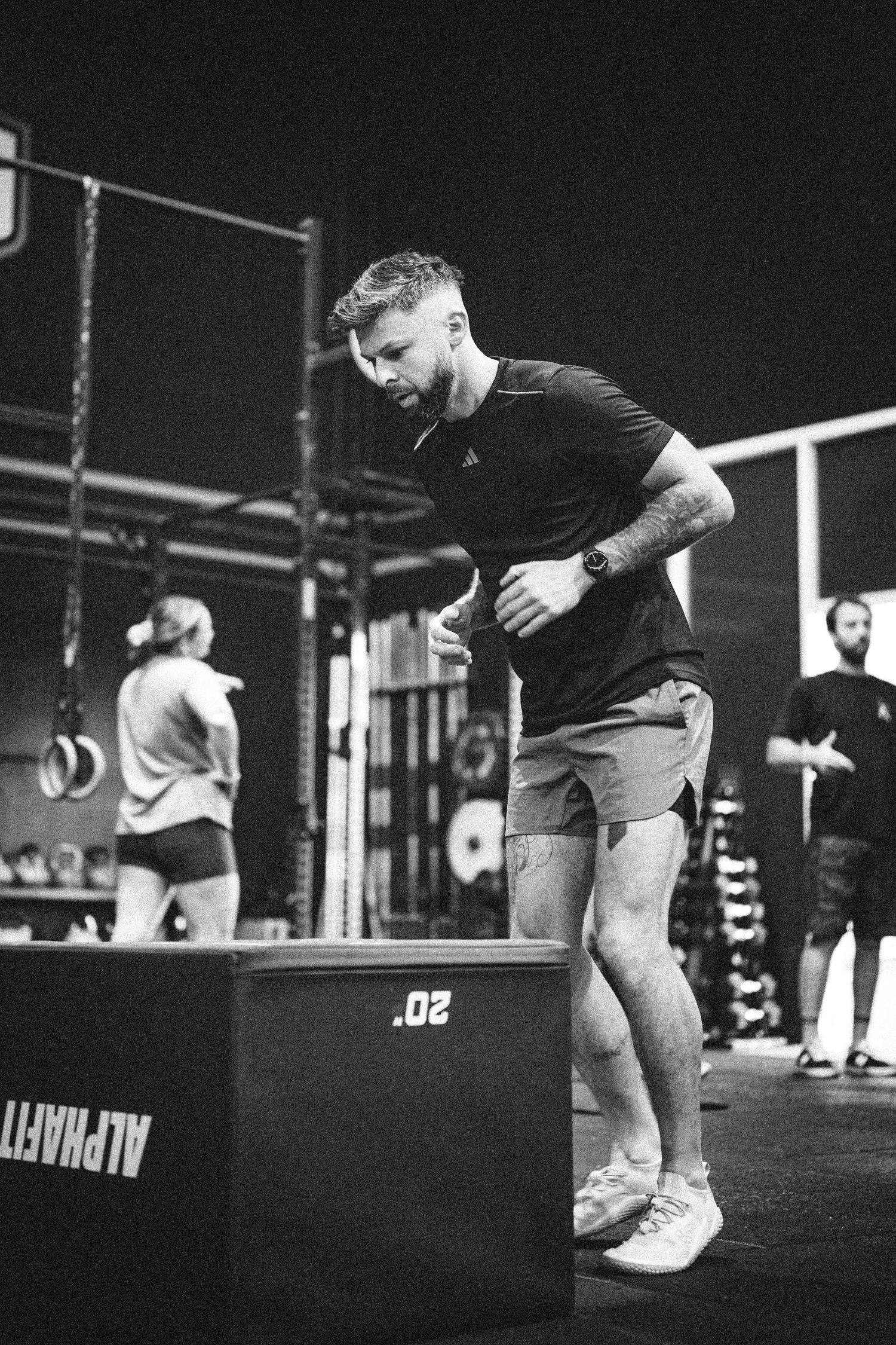 Fit man stepping onto a plyo box during a CrossFit workout in a black and white gym photo.
