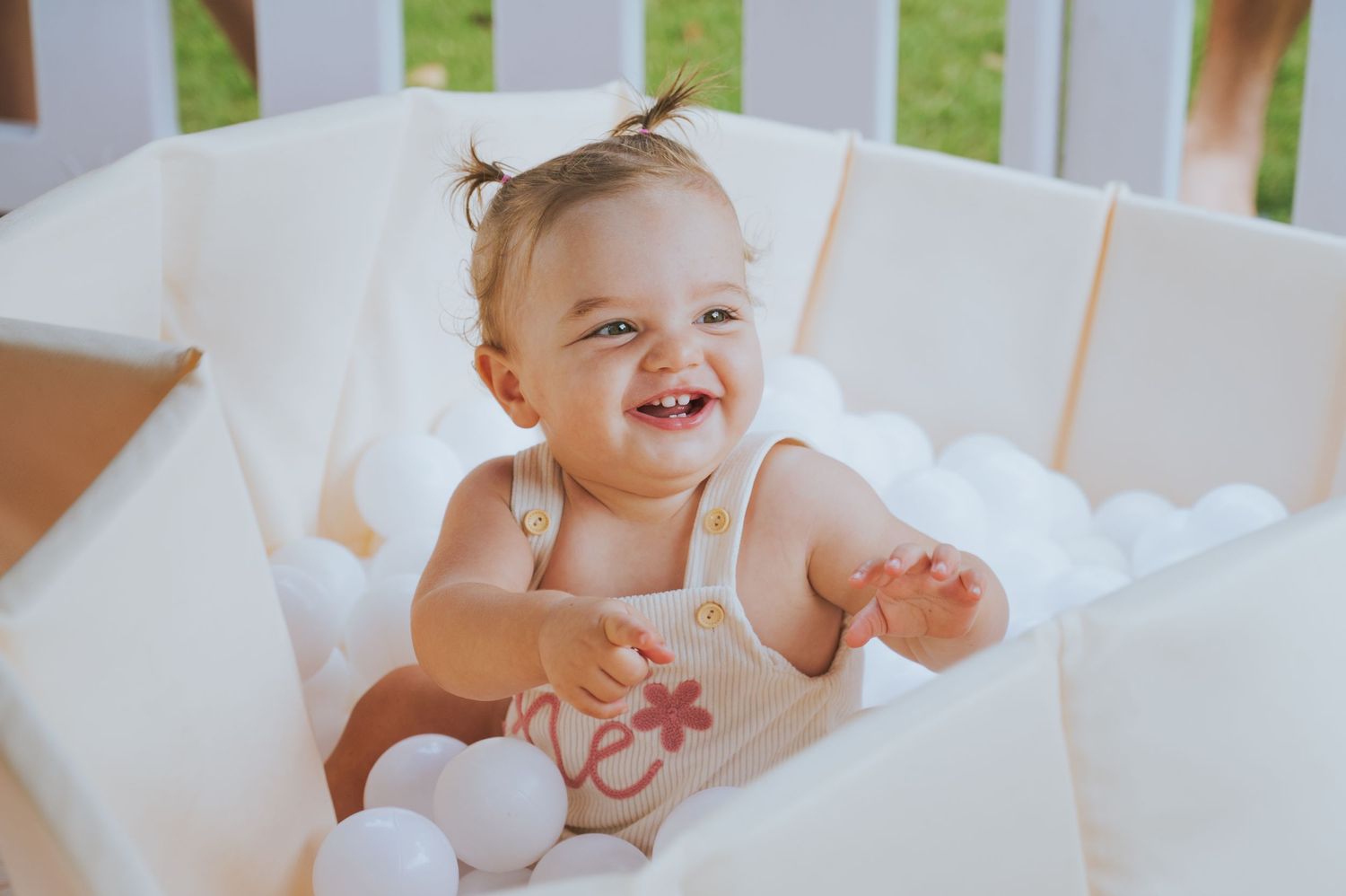 adorable smiling baby sitting in a white ball pit wearing a cute romper.