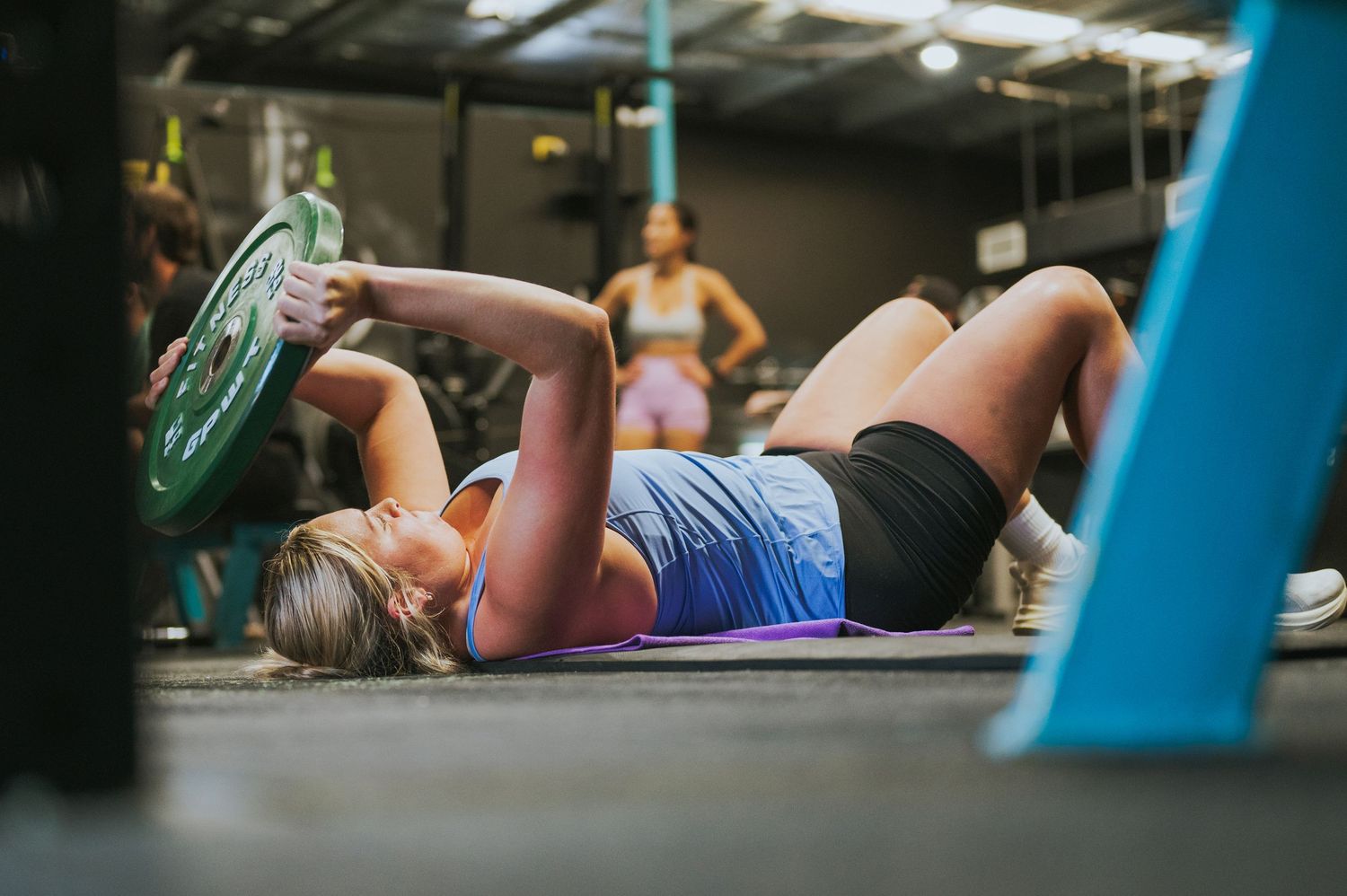 Woman performing floor exercise with weight plate in a vibrant CrossFit gym setting.