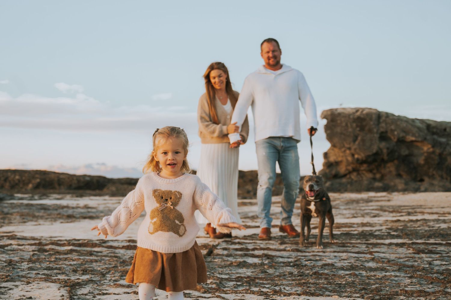 happy family with young daughter and dog enjoying a golden hour beach photoshoot.