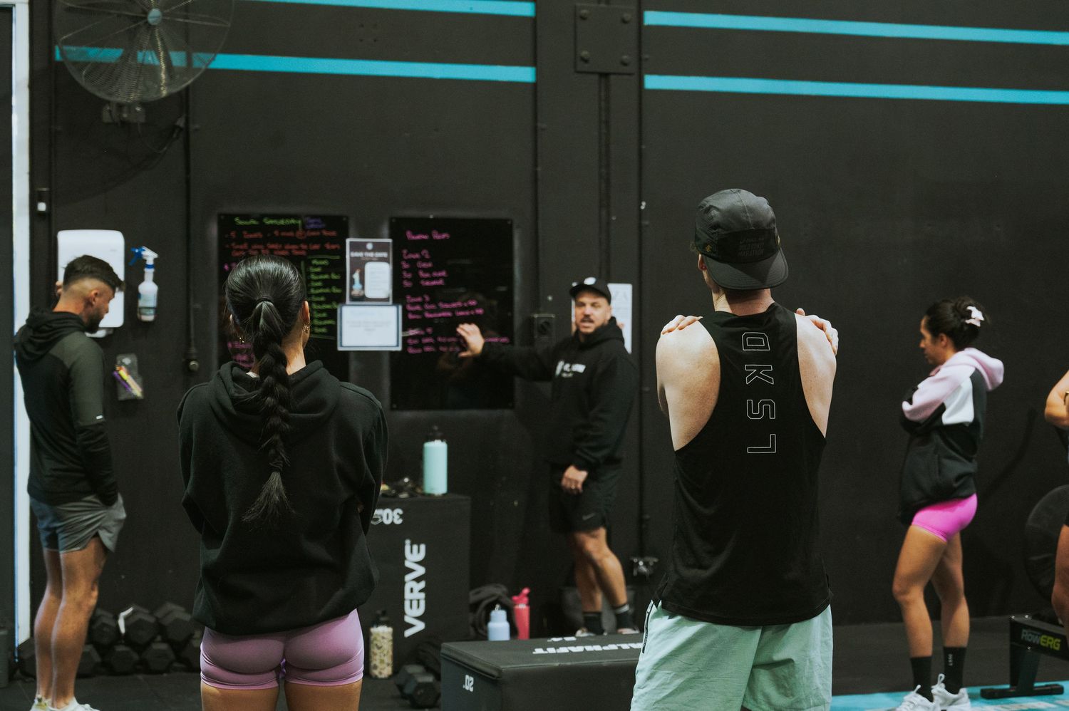 Fitness coach instructing a group of athletes in a modern black-walled gym.
