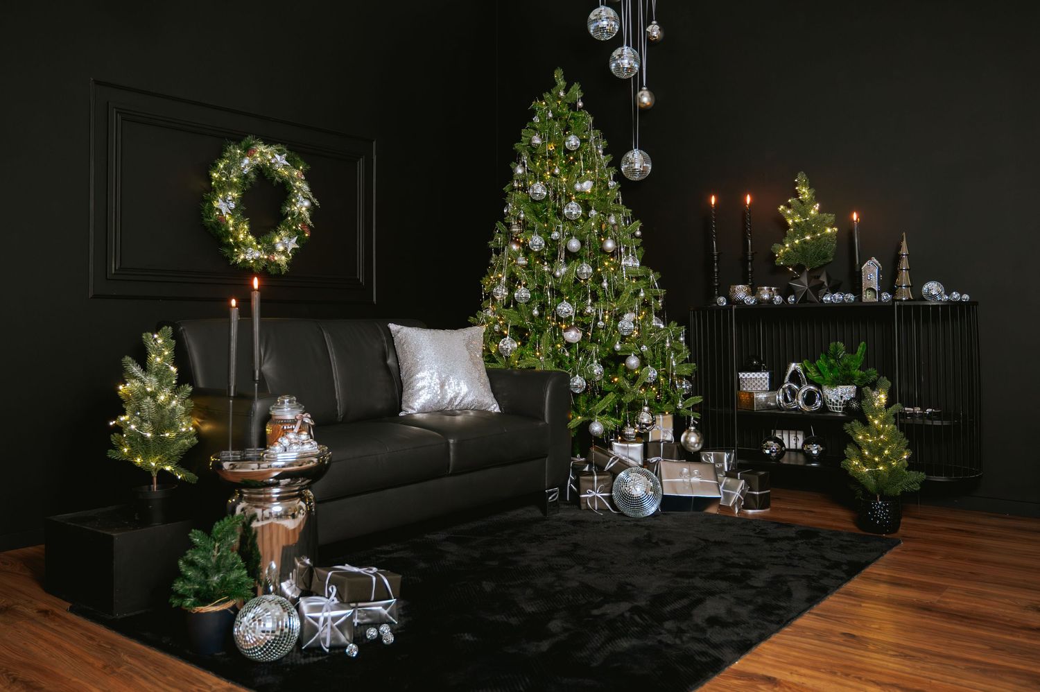 Elegant black living room with a decorated silver and white Christmas tree, lit wreath, gray sofa, mini trees, and holiday mantel decor.