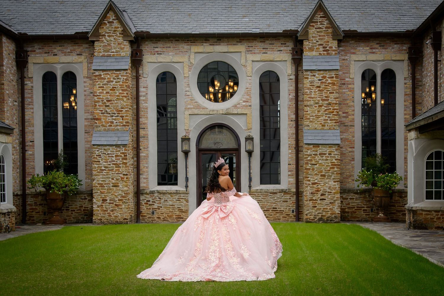 Young woman in pink ball gown quinceañera dress posing in front of stone mansion.