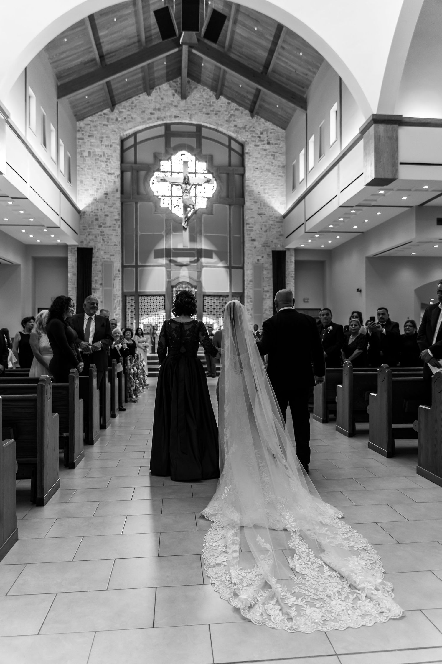 Black and white photo of bride walking down church aisle with long veil.