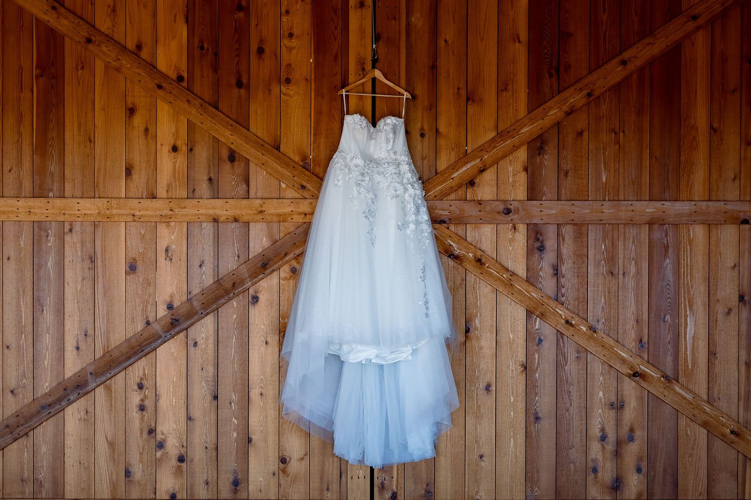 Elegant lace wedding dress hanging on rustic wooden barn doors.