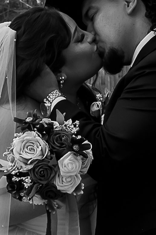 Black and white close-up of bride and groom sharing a kiss, bride holding a bouquet of roses.