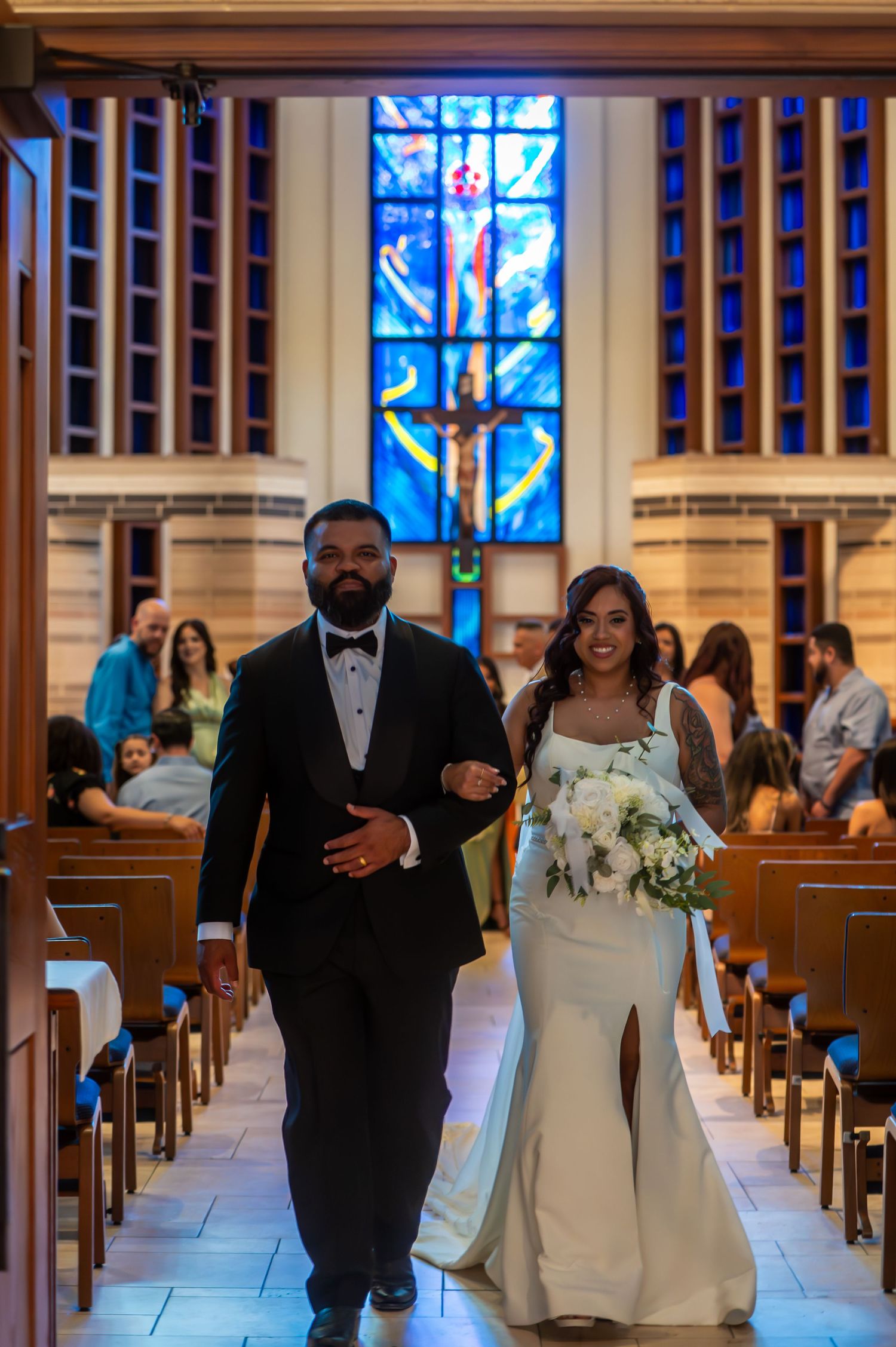 Bride and groom walking back down church aisle after wedding ceremony with stained glass backdrop.
