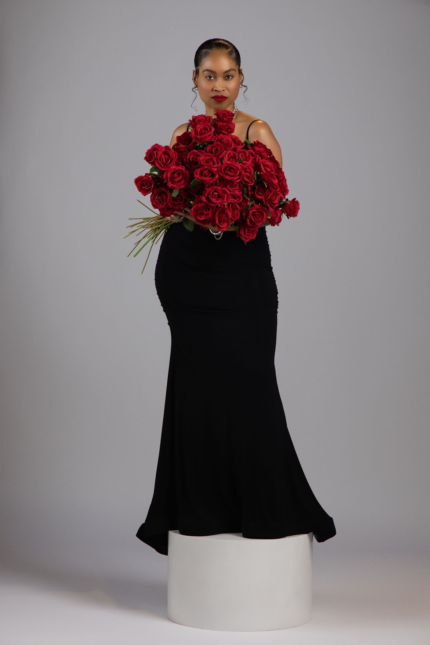Artistic fashion portrait featuring a black dress contrasted with vibrant red roses against a grey backdrop.
