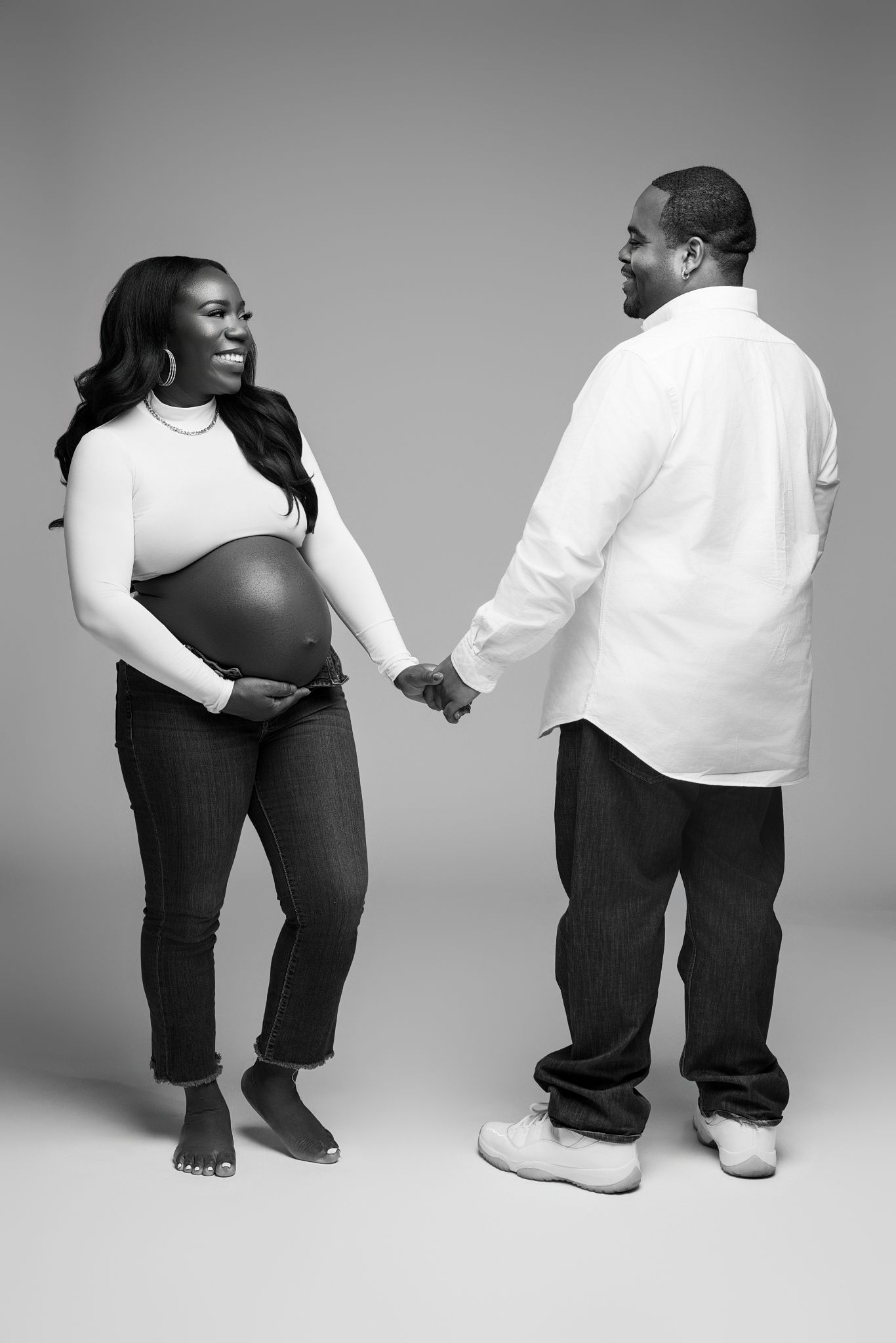 Artistic black and white series showing couple's legs and feet in casual attire against studio backdrop.