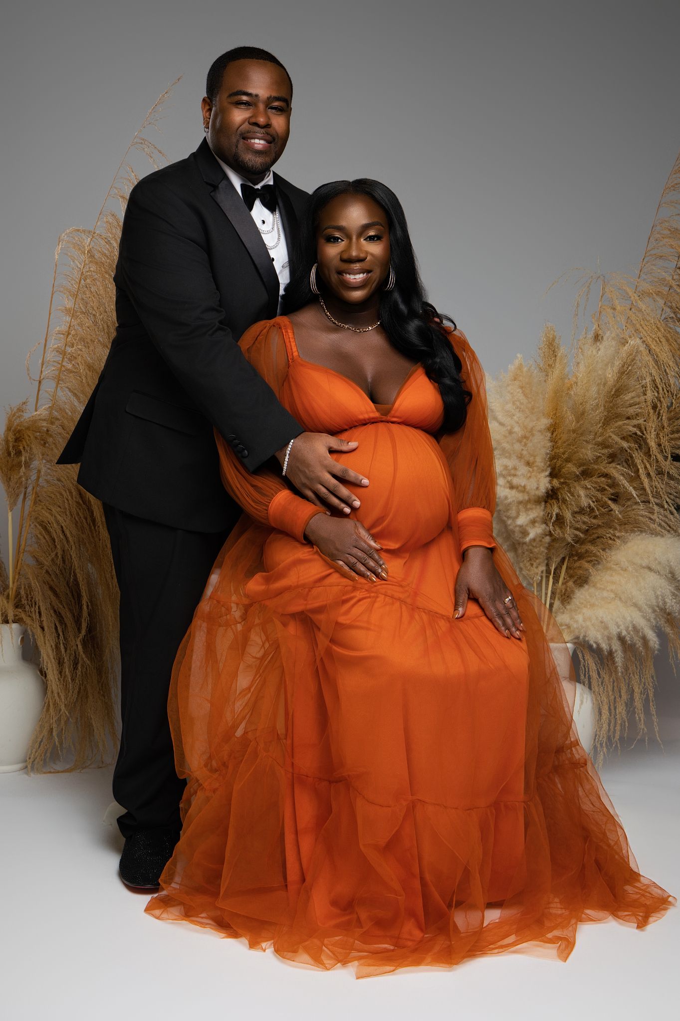 Romantic studio portraits featuring a couple with pampas grass decor and flowing orange gown.