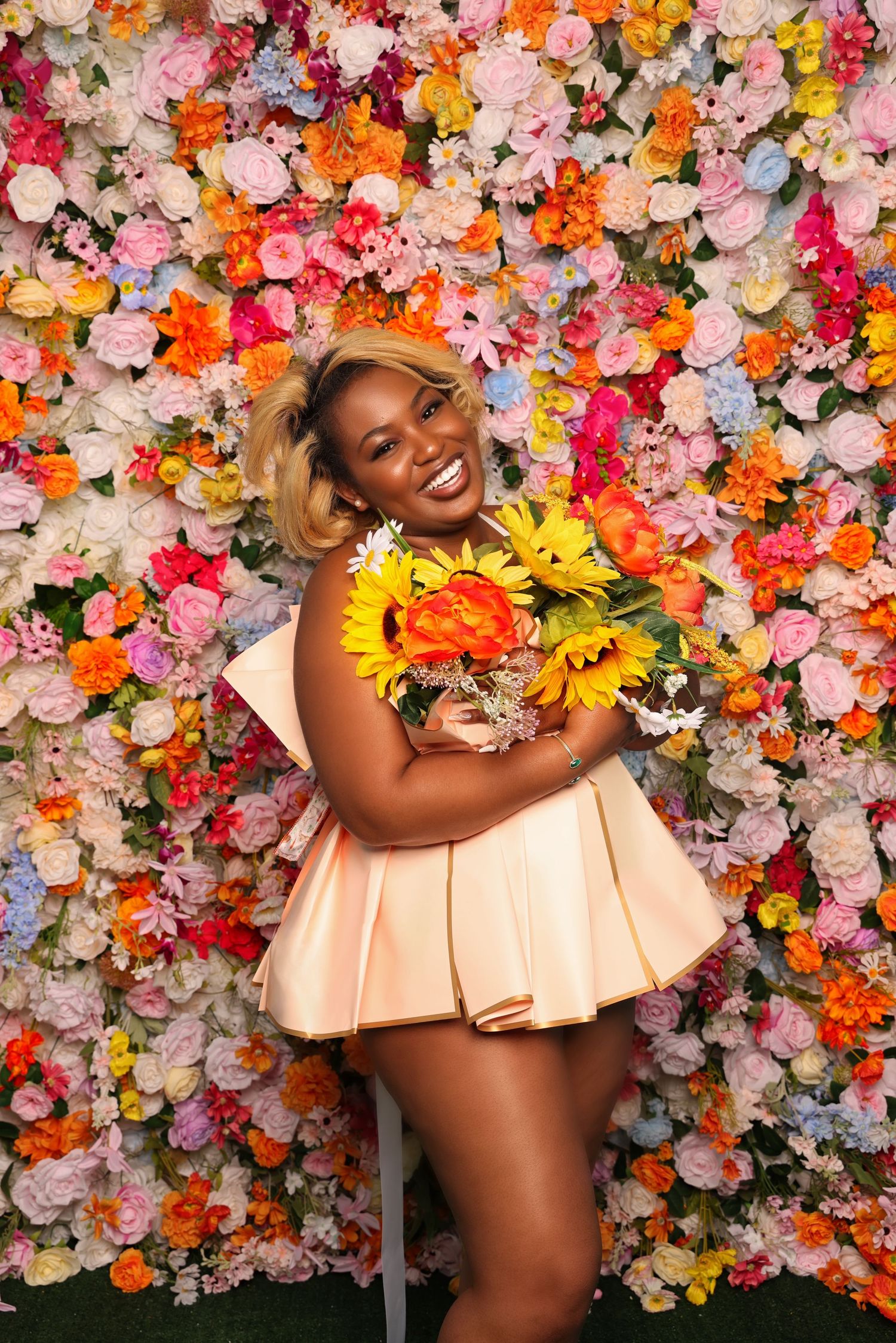 Joyful portrait with sunflowers against a colorful flower wall in a peach dress.