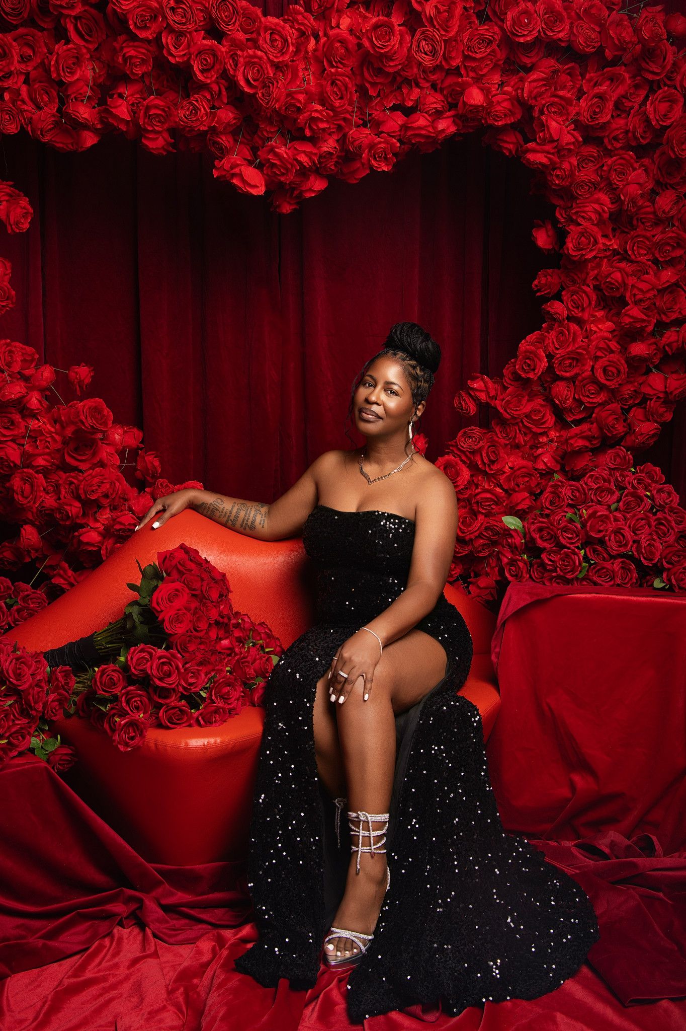 Glamorous photo shoot against backdrop of red roses featuring model in sparkling black gown striking elegant poses.