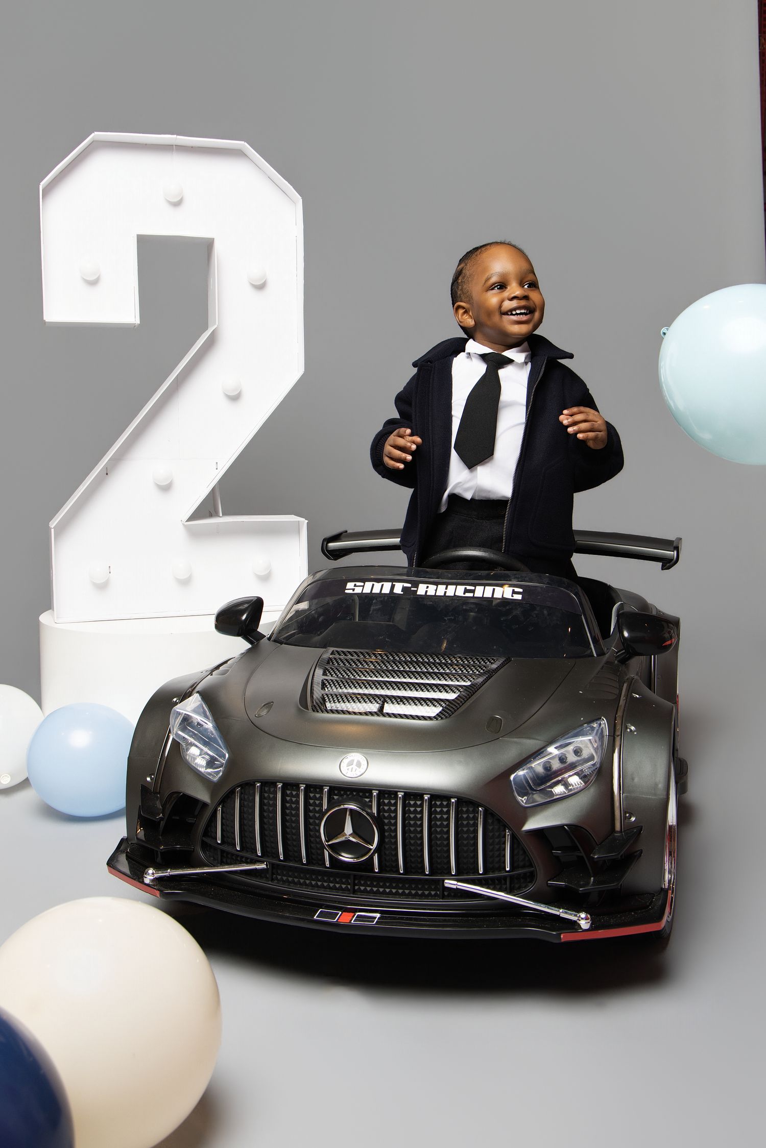 A child rides in a small black Mercedes toy car with multiple views showing their joyful expression and the car's details.