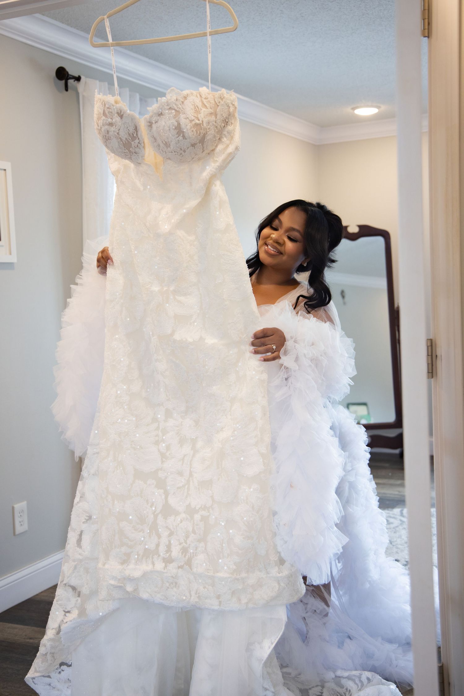 A beautiful white lace wedding dress with sweetheart neckline hangs on display in a bright dressing room.