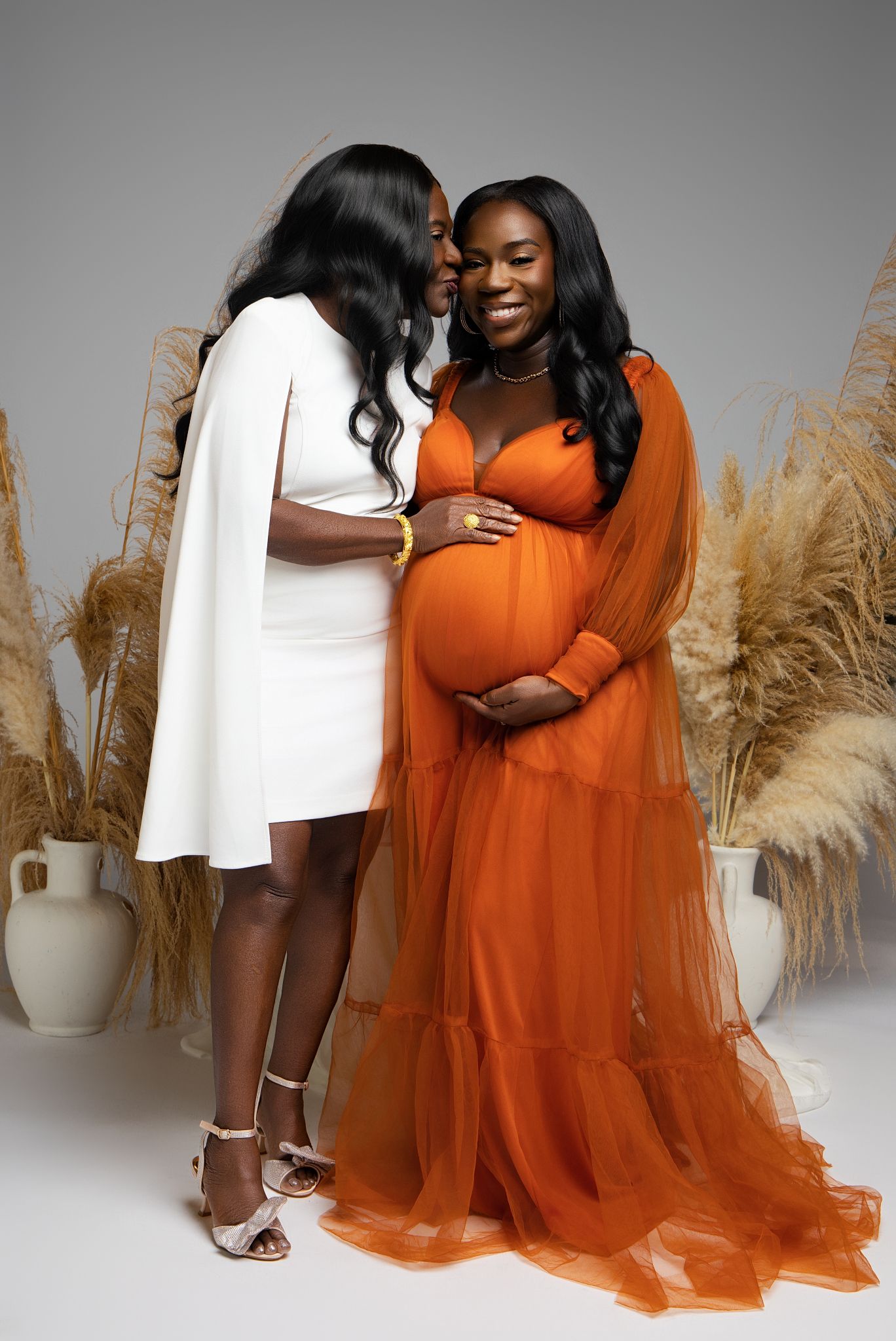 Maternity photo series showing couple in orange tulle dress and white outfit against pampas grass backdrop.