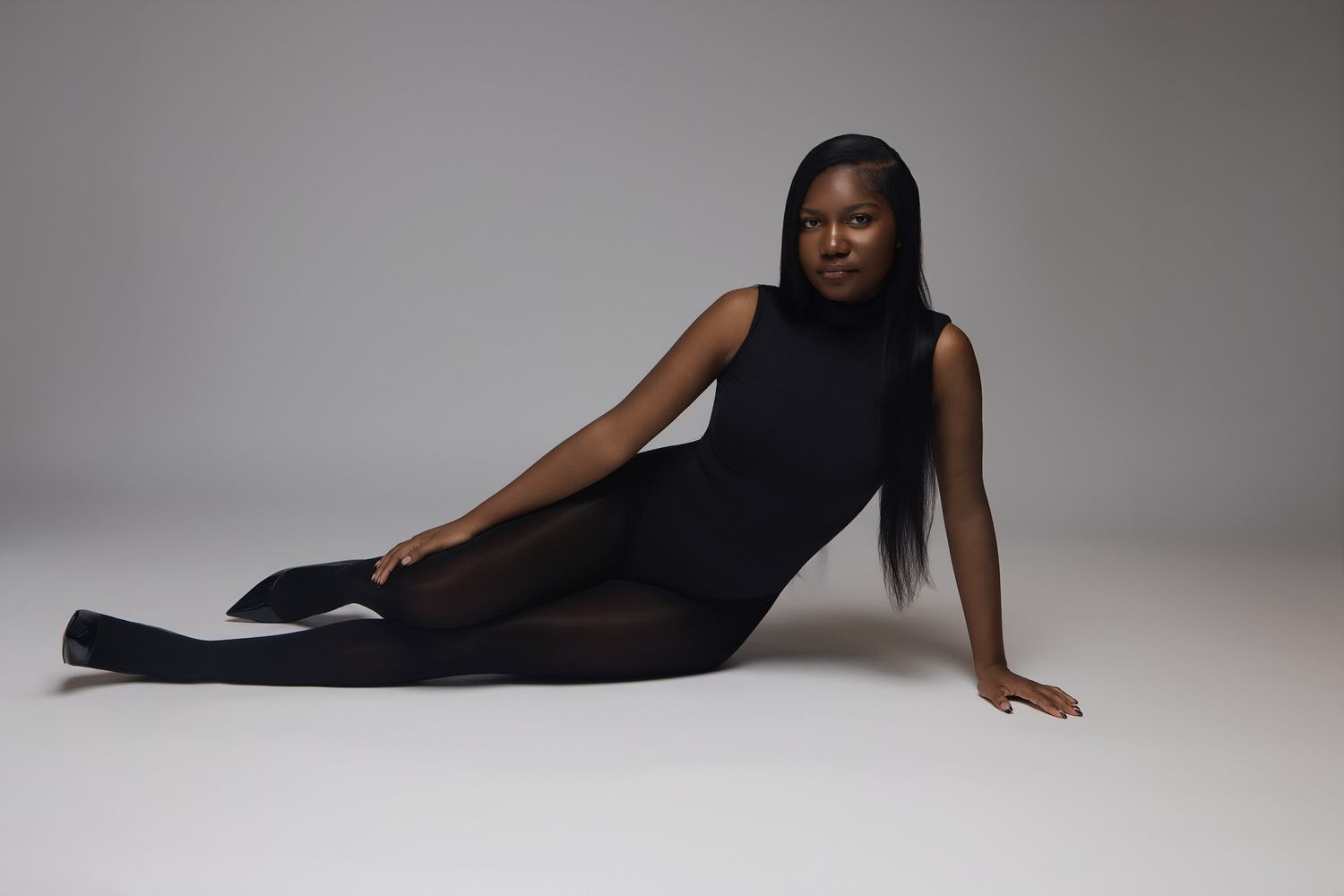 A figure in a sleek black outfit poses elegantly on a white studio floor in multiple artistic positions.