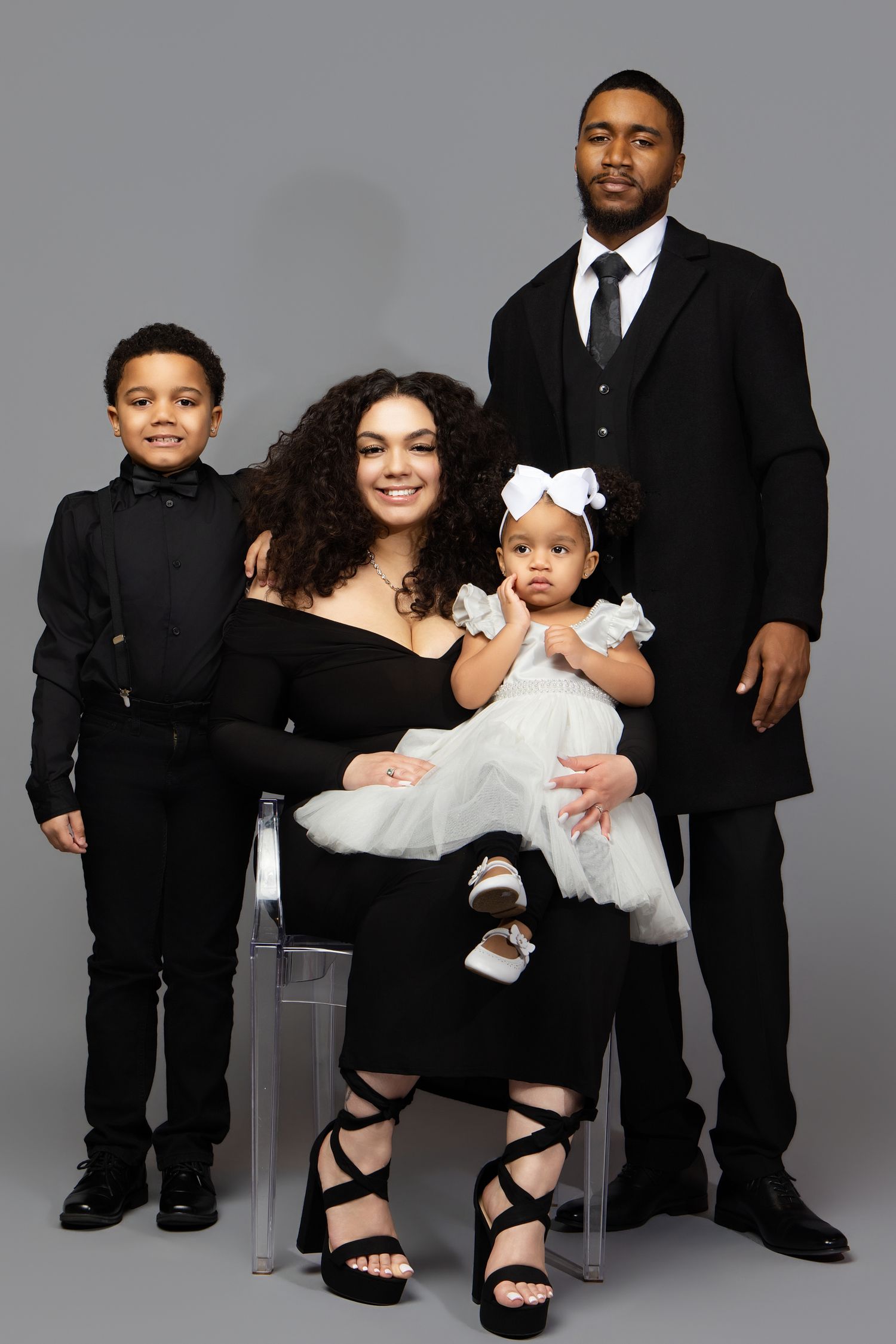 A family portrait series in black and white attire showing progressive poses against a gray studio backdrop.