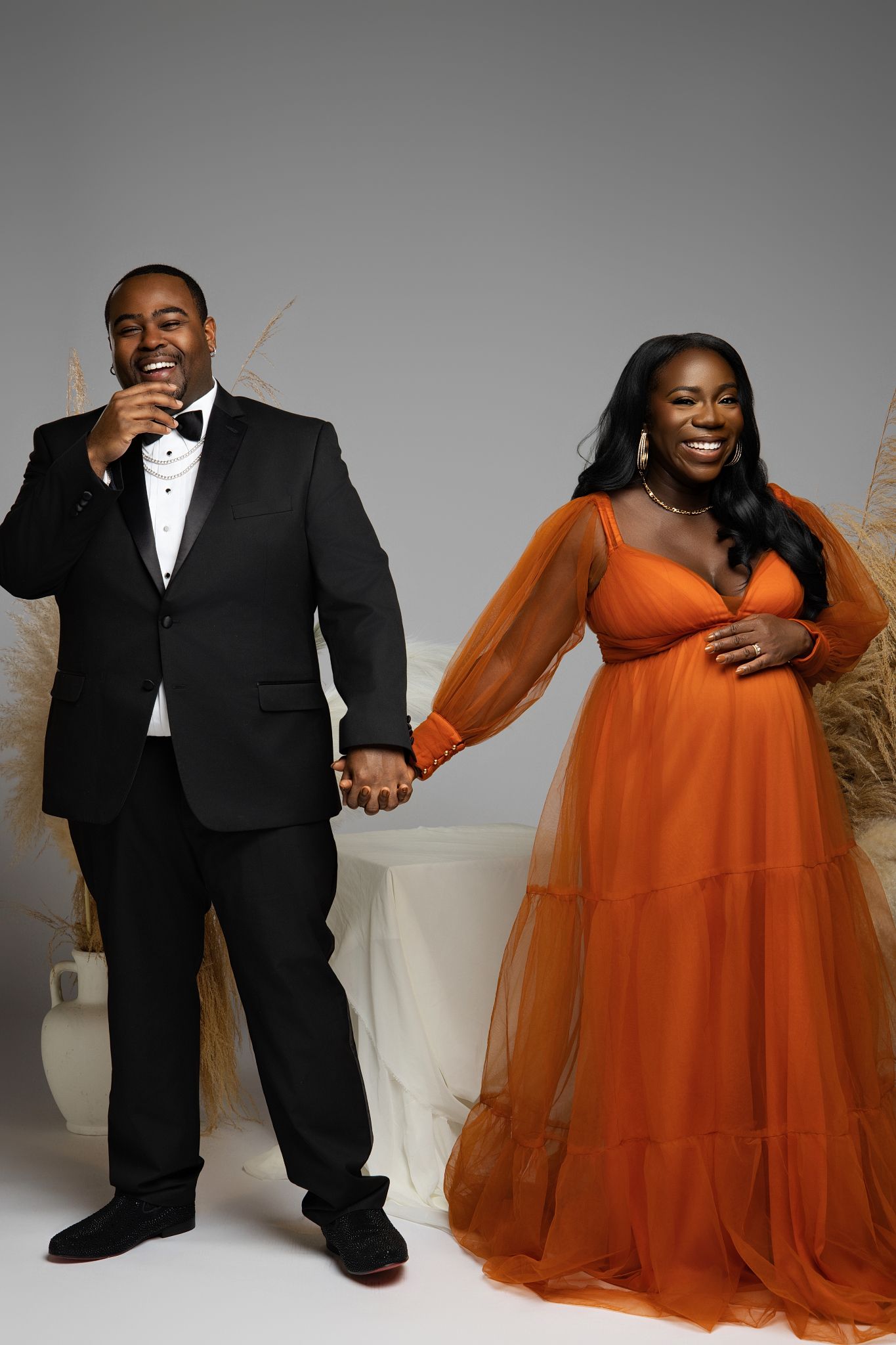 A couple shares joyful moments in formal wear with orange tulle gown and black tuxedo during a photo session.