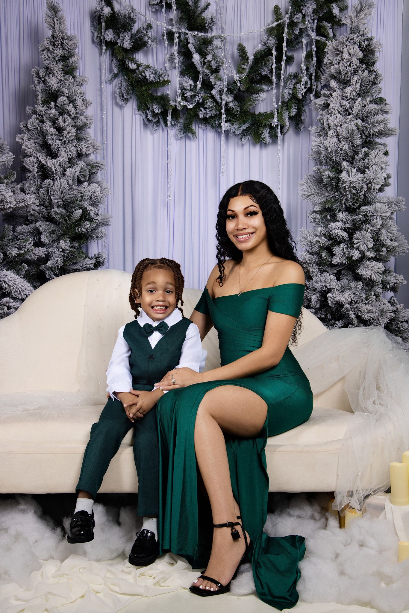 Winter holiday photoshoot setup with snow-covered pine trees and white couch against purple backdrop.