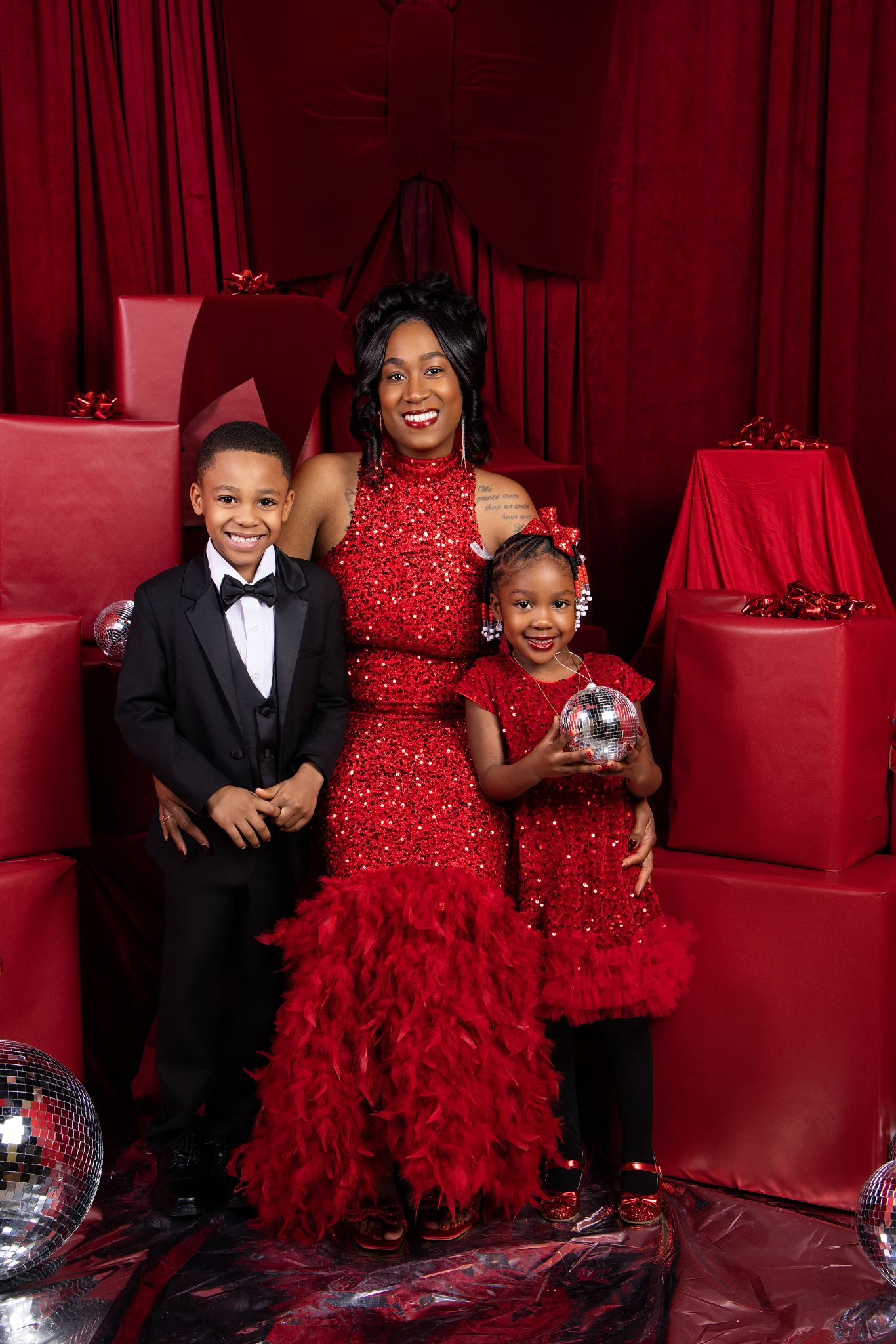 Three people pose in coordinating red formal attire against a red backdrop for a glamorous photo session.