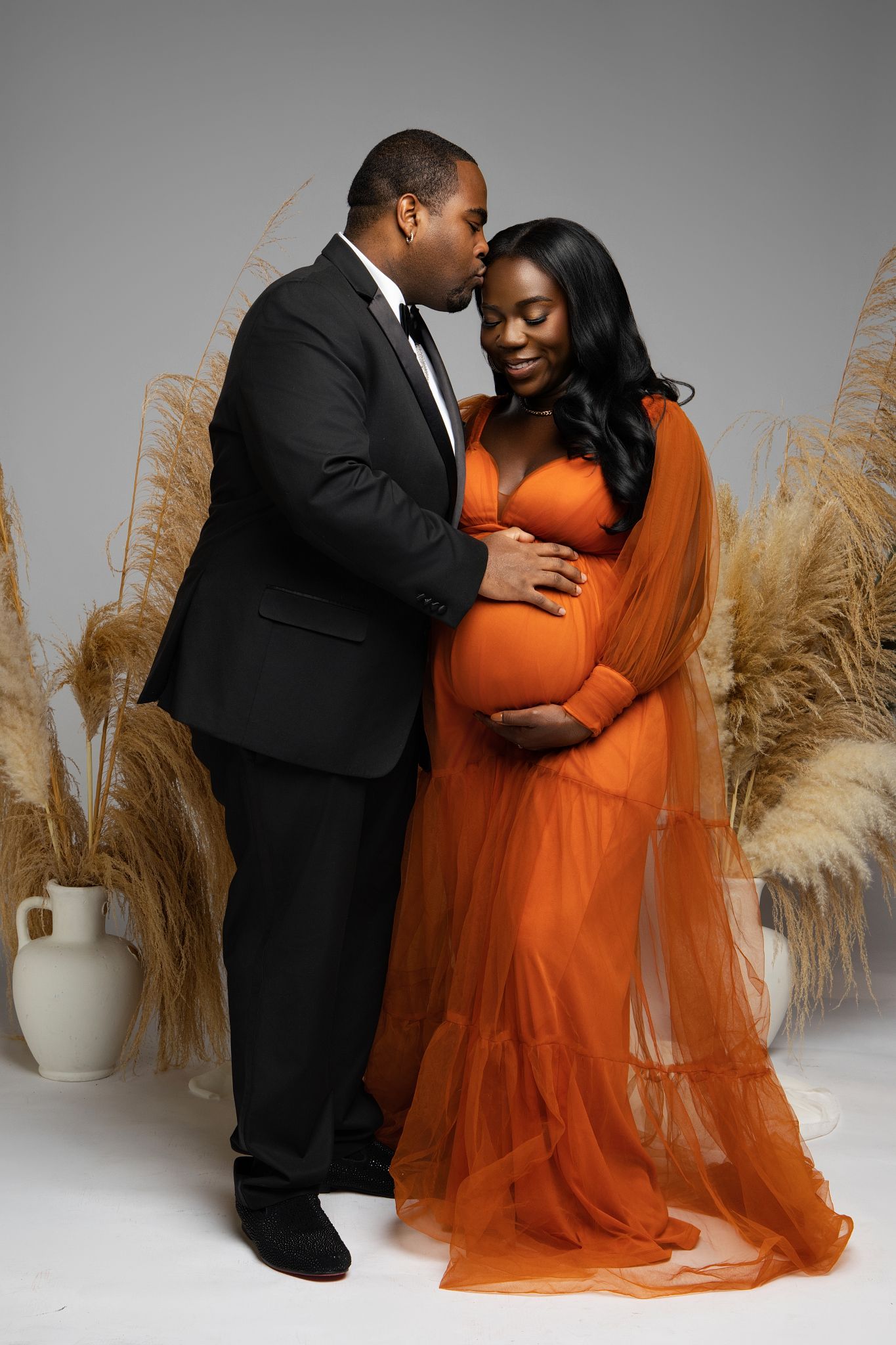 Intimate couple's photoshoot with orange tulle dress and pampas grass decorative elements.