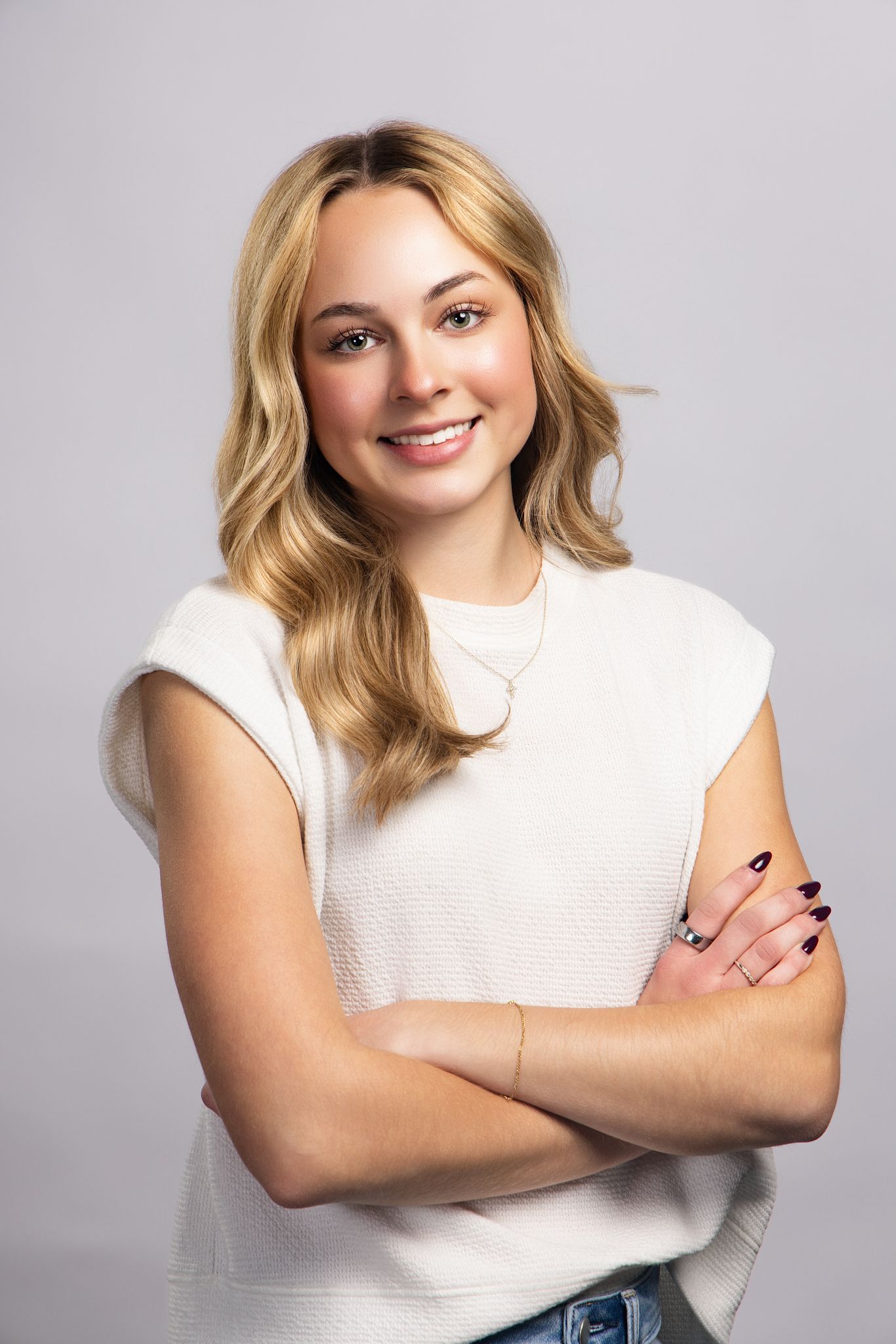 Professional studio portrait series of a person in a white sleeveless top posing with crossed arms against a light background.