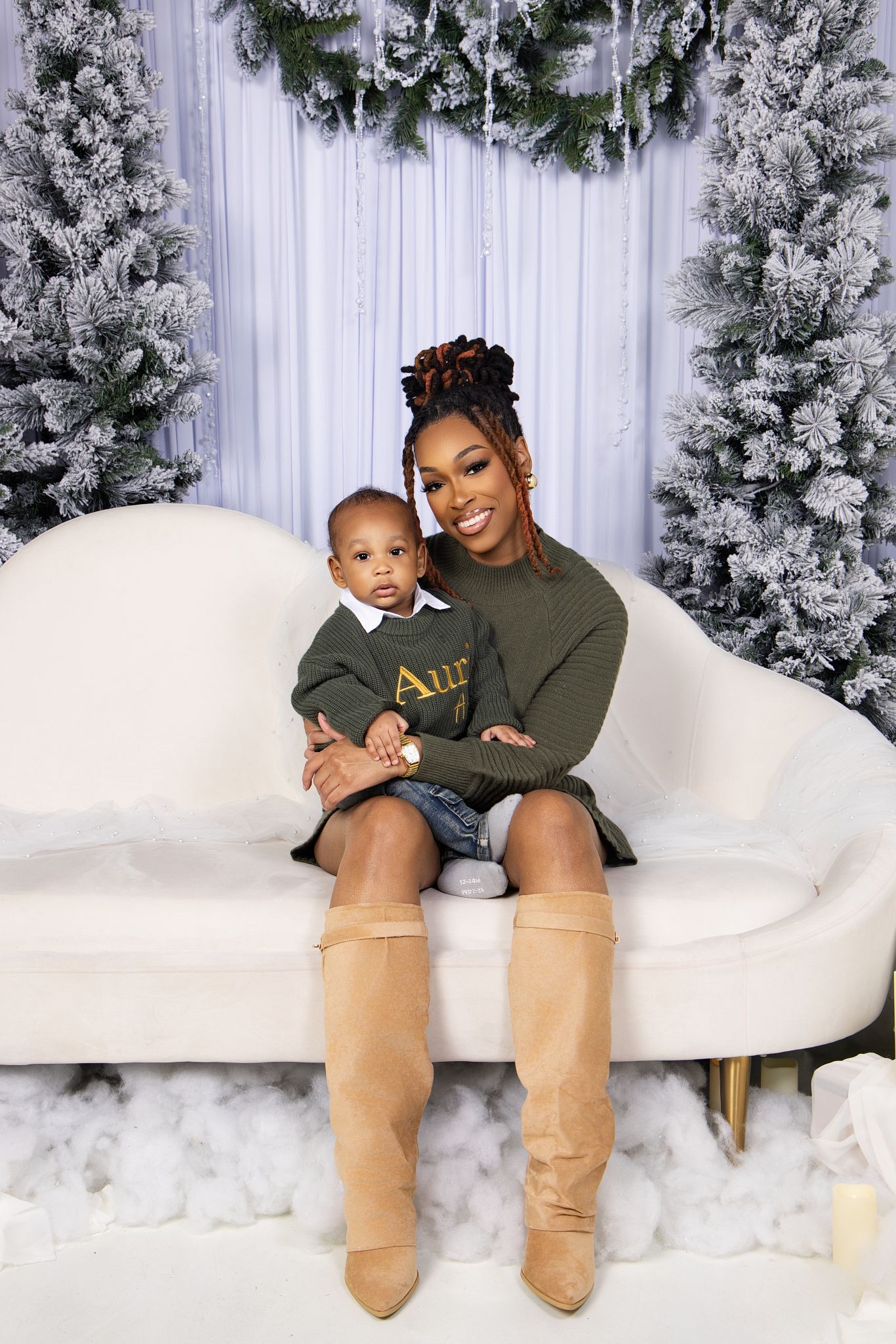 A cozy winter photo series with matching olive sweaters and tan boots against a snowy white backdrop with flocked trees.