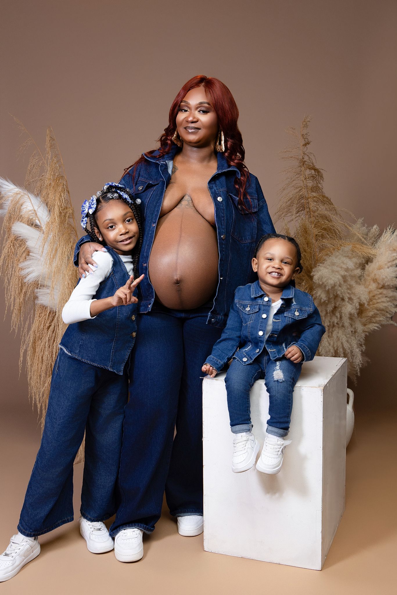 Mother and child wearing matching denim outfits pose together in studio with pampas grass decorations.