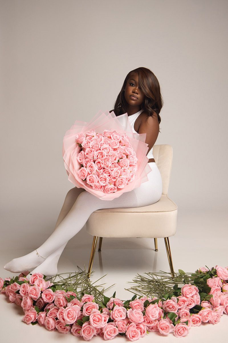 Artistic fashion photo with pink roses scattered on floor near white chair and figure in white outfit.