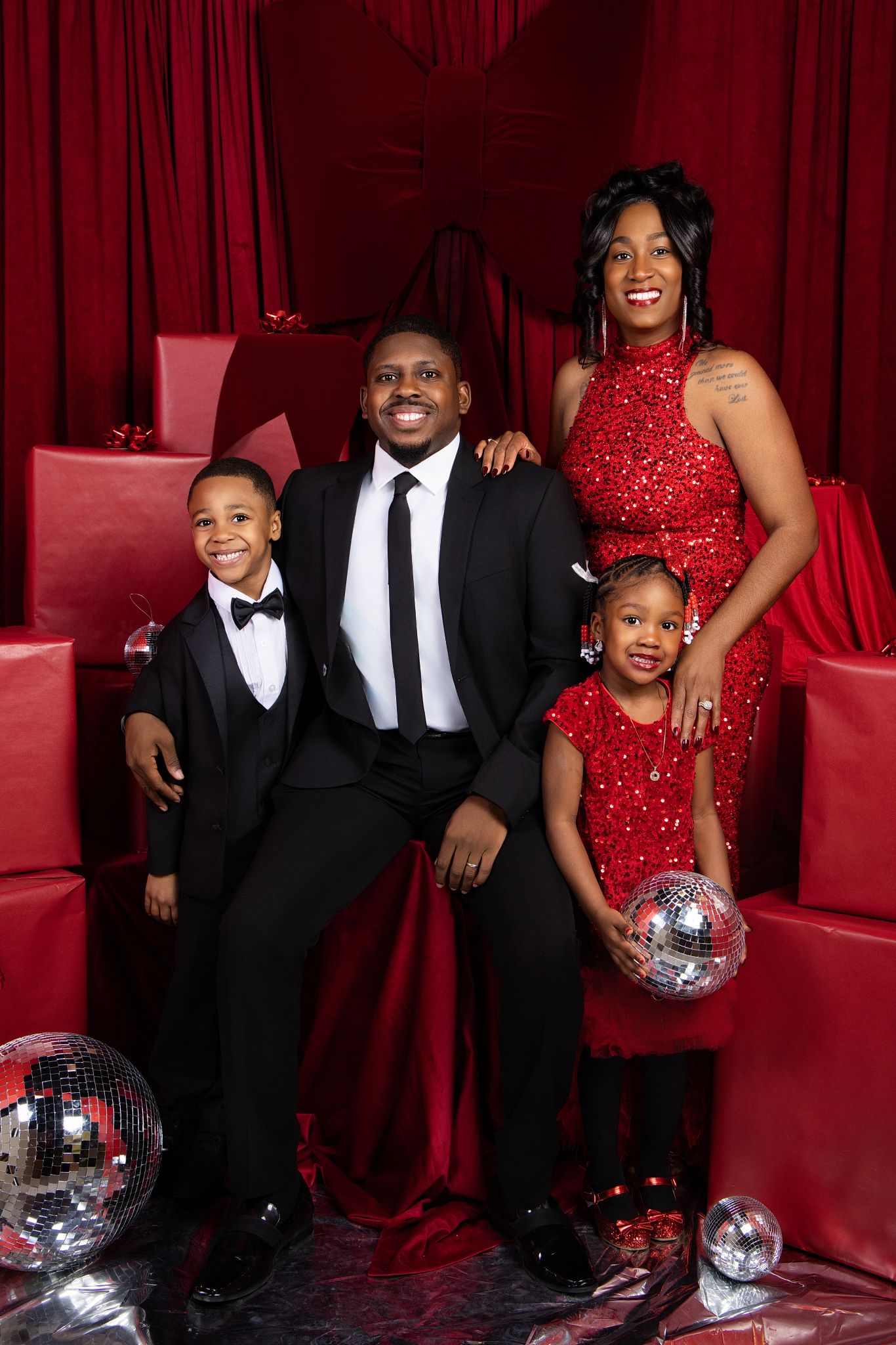 A family poses in formal attire against a red curtain backdrop with a disco ball for a glamorous photo shoot.