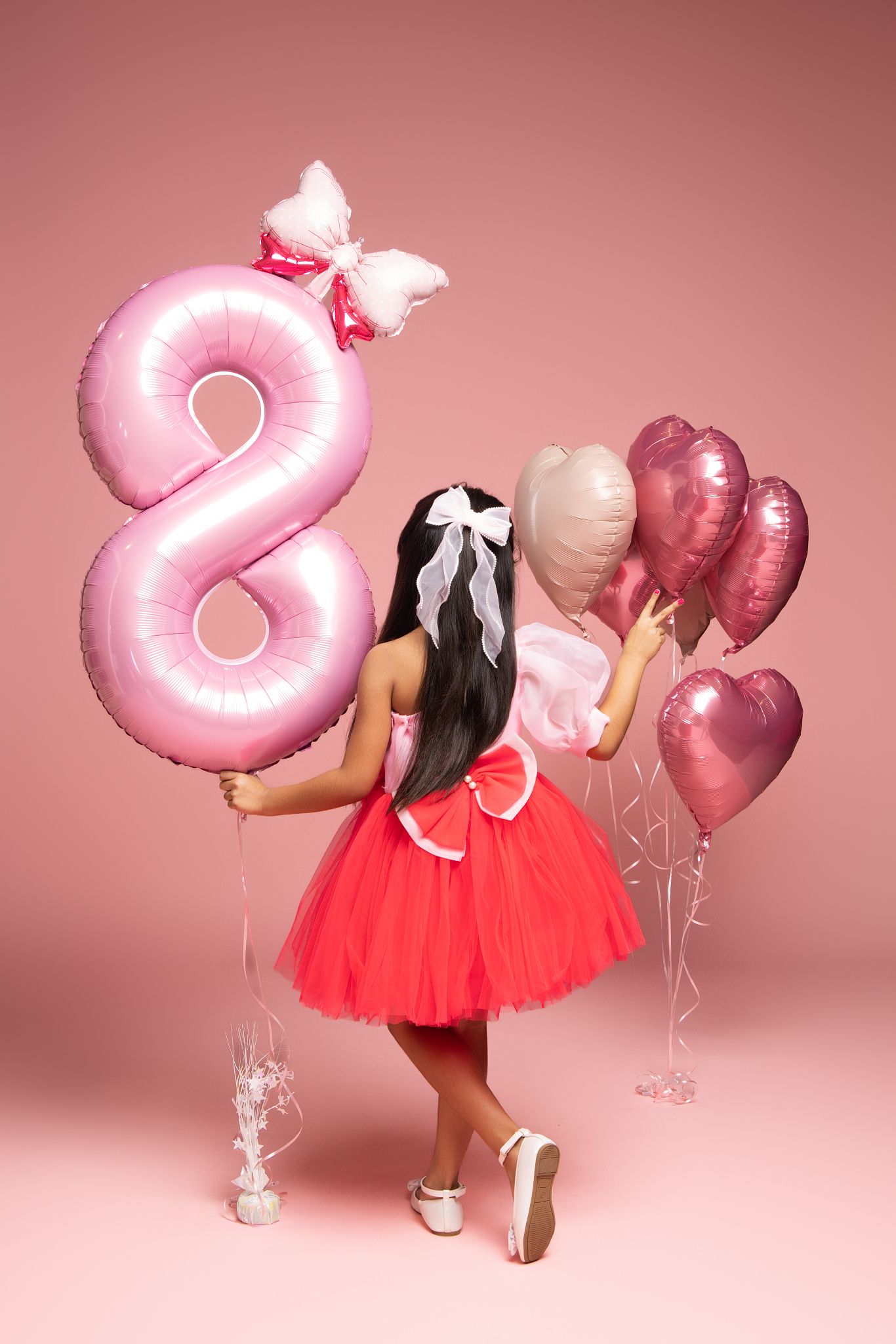 A festive birthday setup with a large pink number 8 balloon and heart-shaped balloons against a pink backdrop.