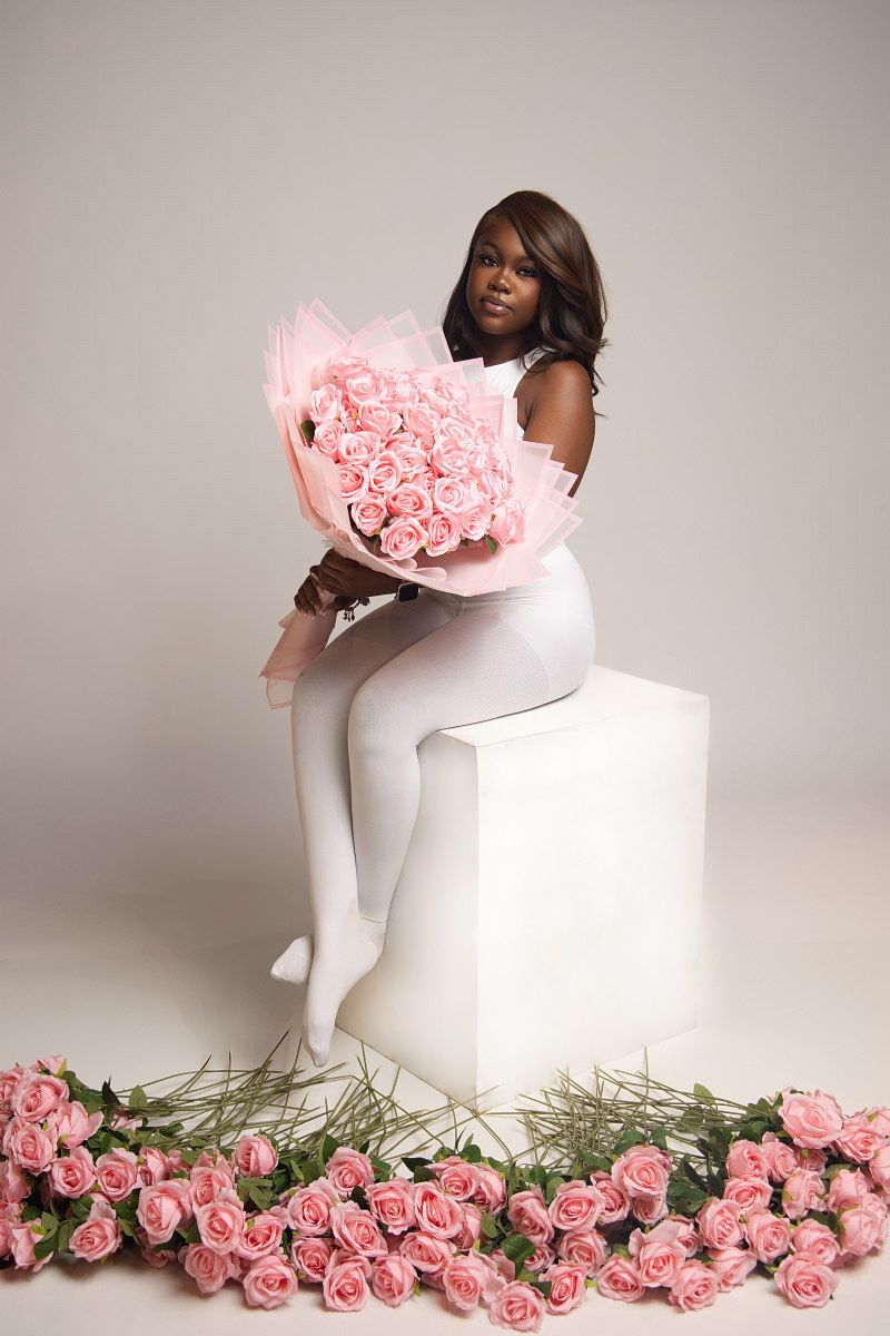 Minimalist fashion scene with pink roses and white cube featuring elegant pose in white attire.