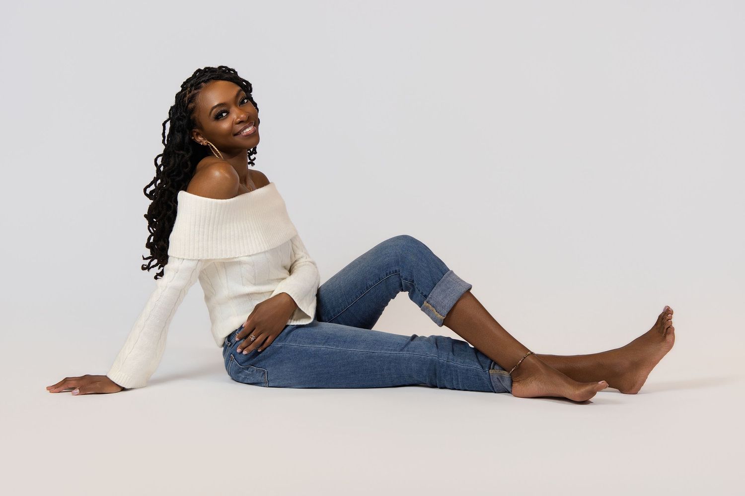A woman in a white sweater and blue jeans relaxes in various casual poses against a light gray background.