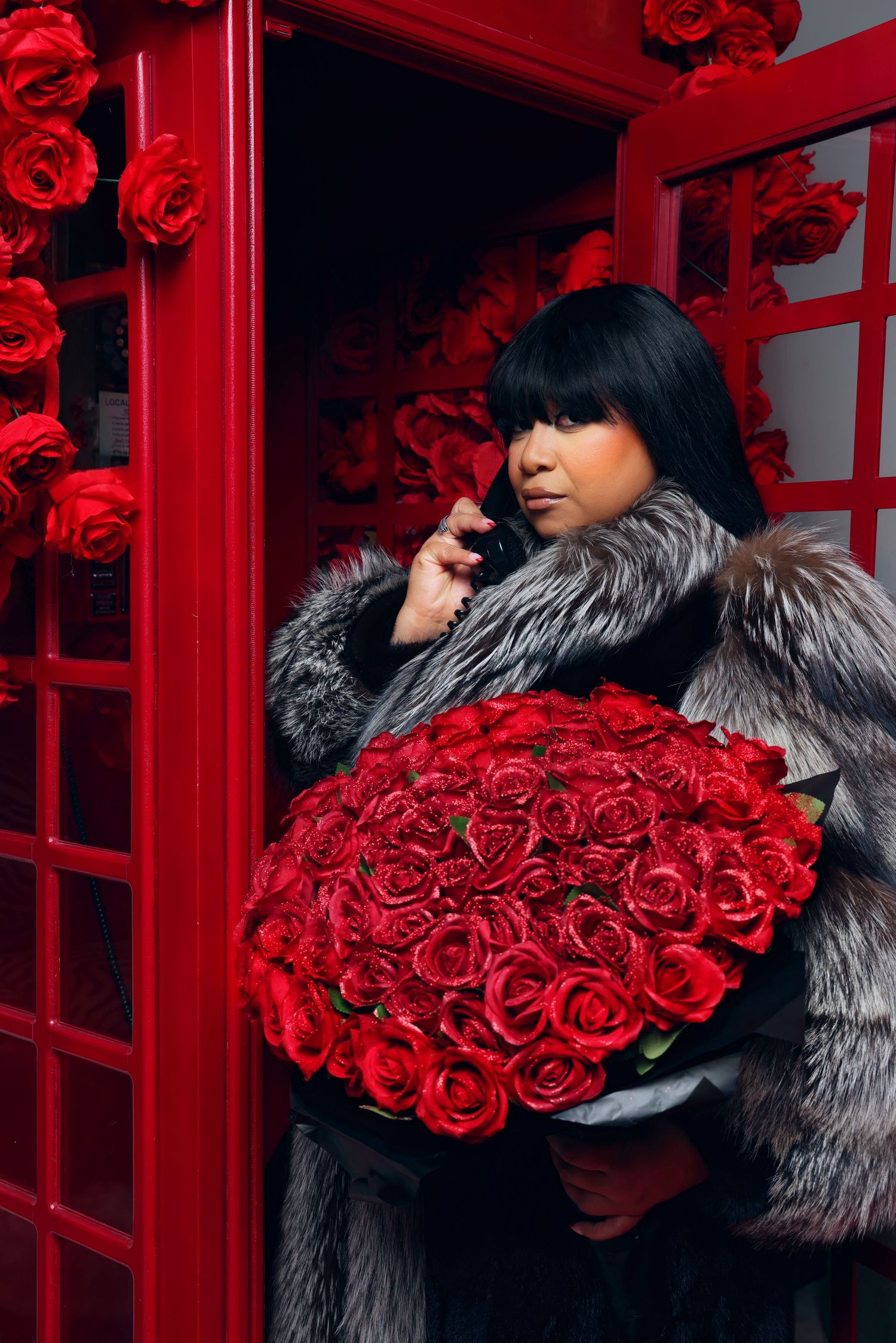 Glamorous shot with fur coat and red roses by red phone booth.