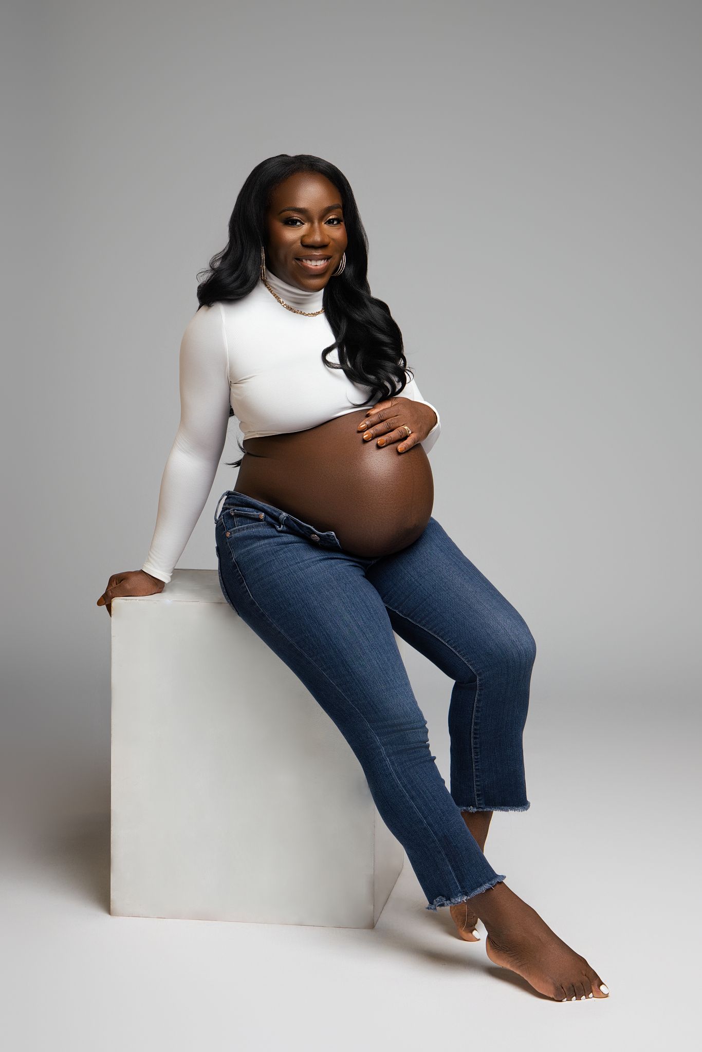 Maternity photography series showing casual denim and white outfit poses against studio backdrop.
